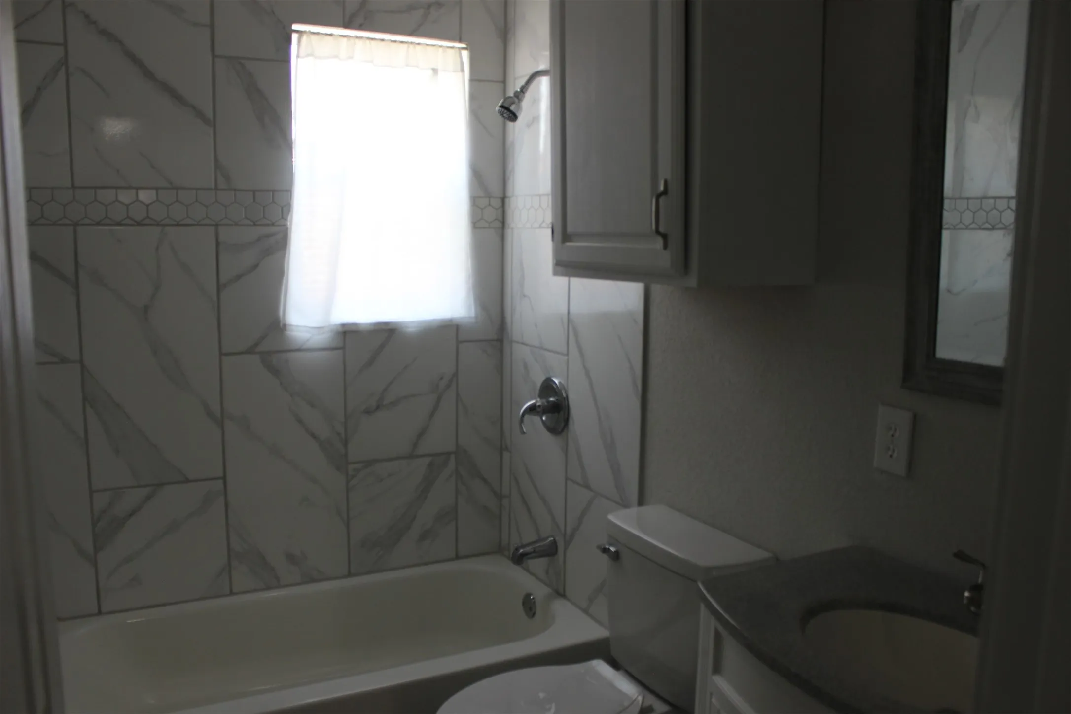 Full bathroom featuring a white bathtub with a shower head and a window