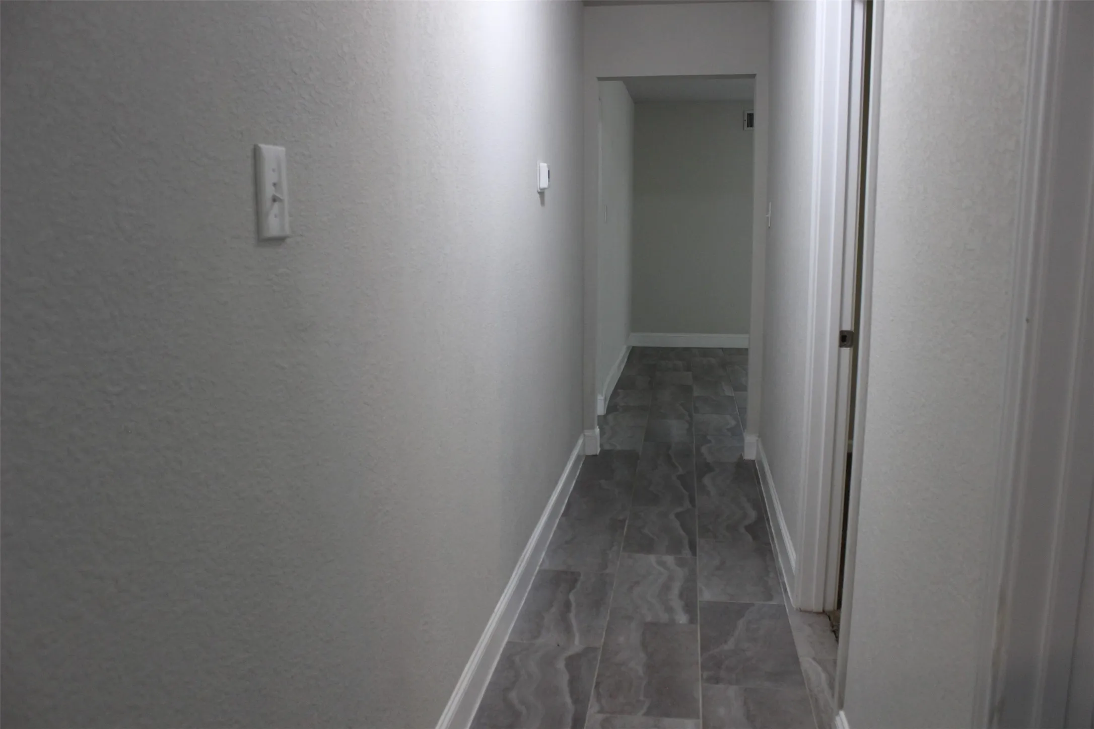 Hallway featuring gray-toned flooring, white baseboards, and light neutral wall paint