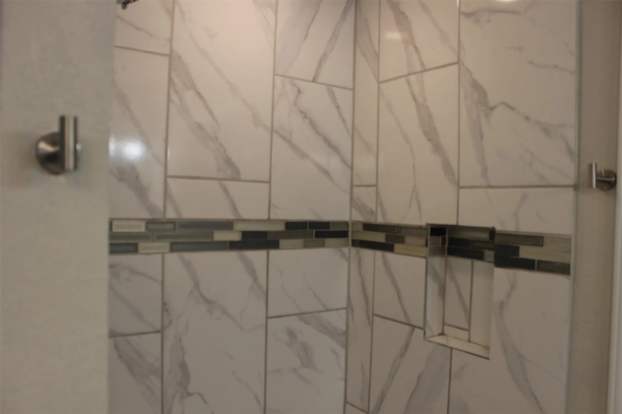 Shower enclosure featuring large format white and gray veined tile
