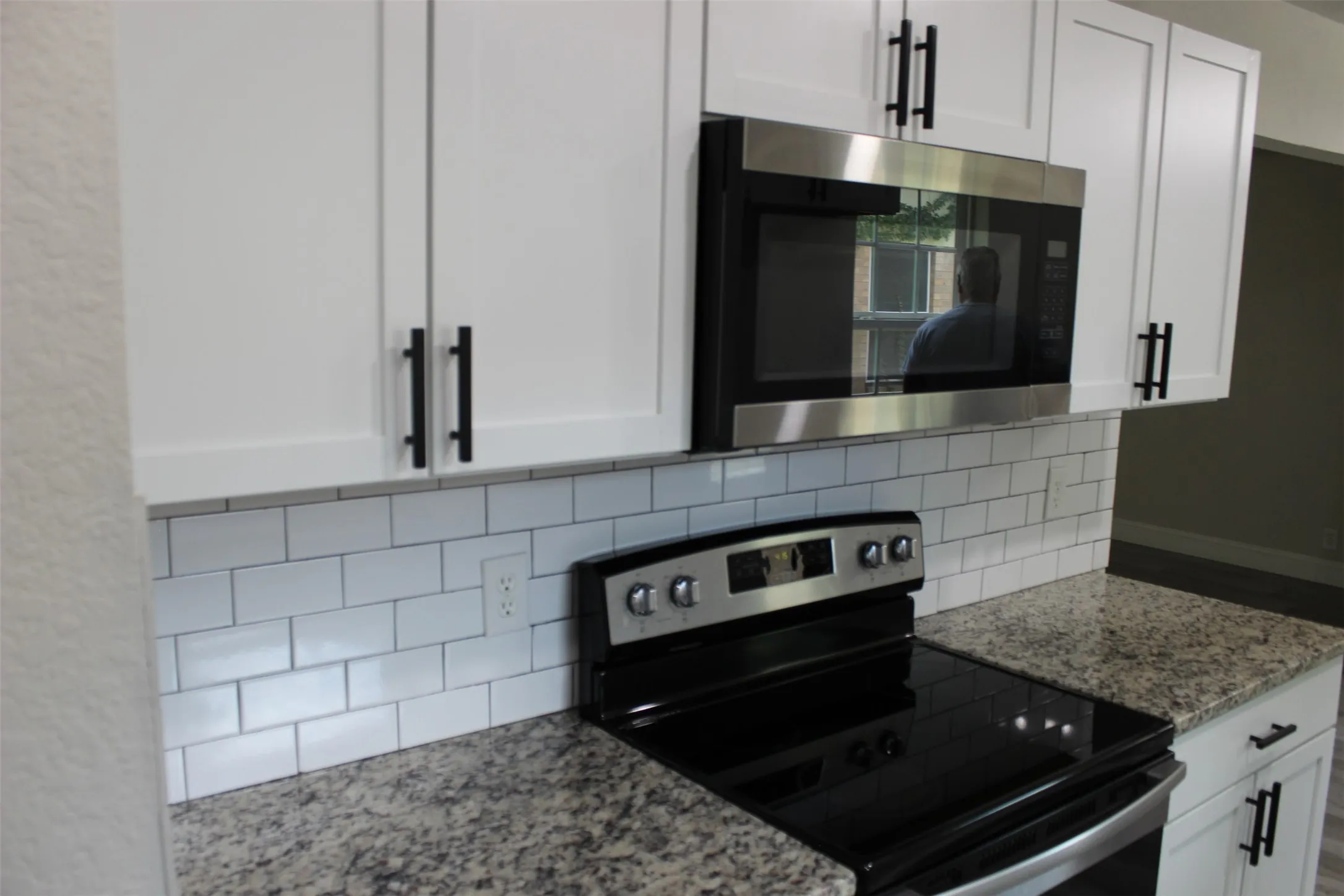 Contemporary kitchen featuring white cabinetry, black hardware, subway tile backsplash, and stone-finish countertops