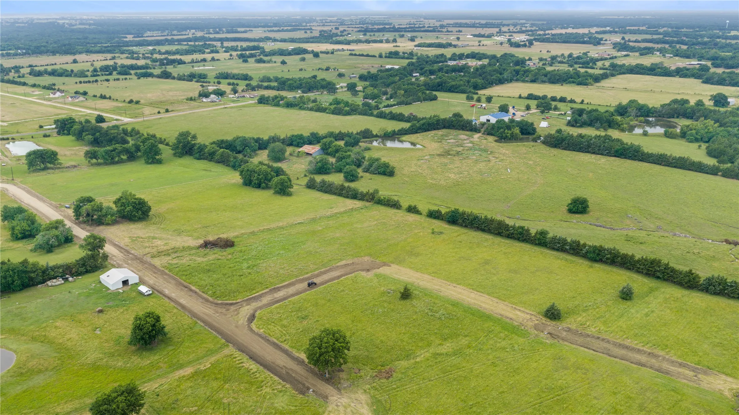 Expansive green pastures with mature trees and a pond