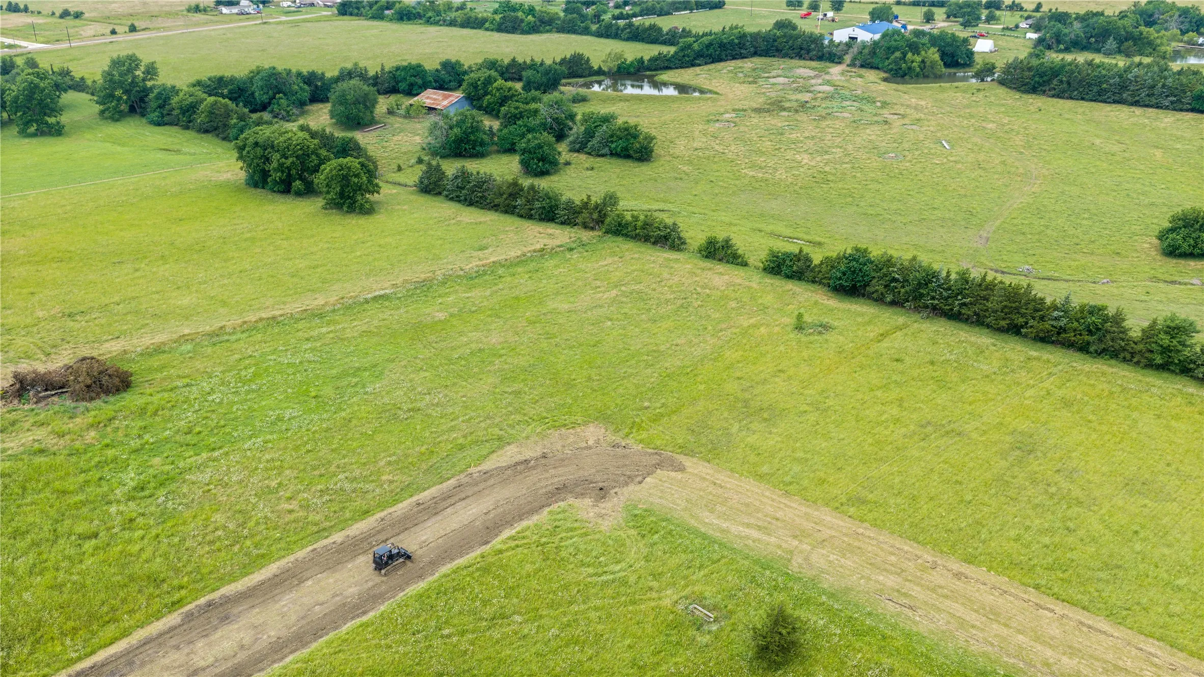 Expansive green acreage featuring a large pond, perimeter treeline, and open fields