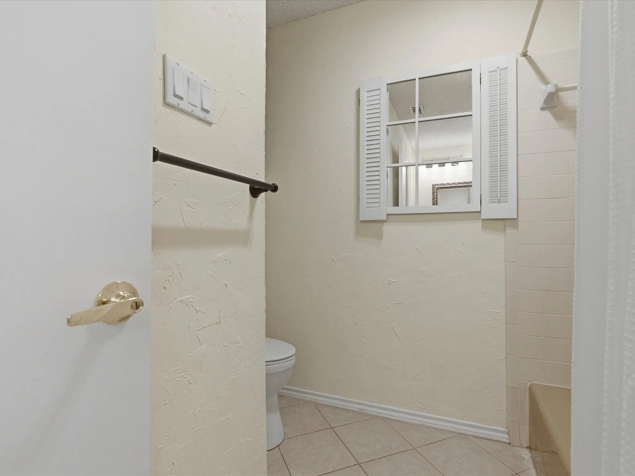 Bathroom featuring a window-style mirror with decorative shutters, tiled flooring, textured walls, a shower with tiled surround, and a built-in shower bench