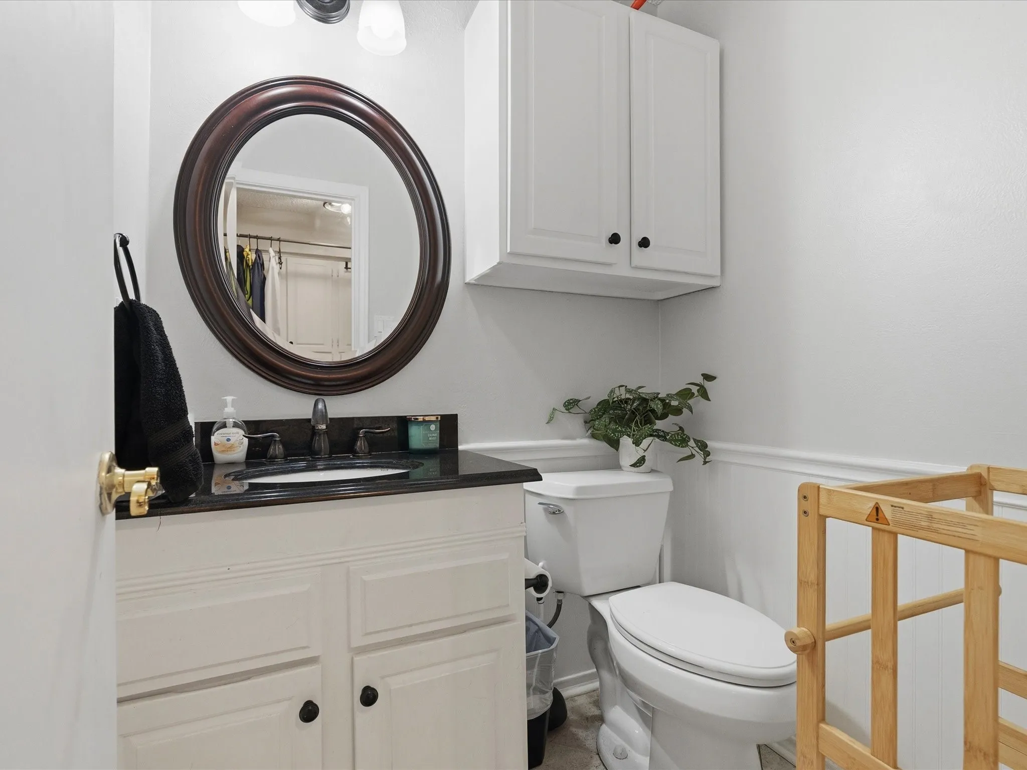 Bathroom featuring a white vanity with dark countertop, an oval mirror with a dark wood-finish frame, and white wall-mounted cabinetry