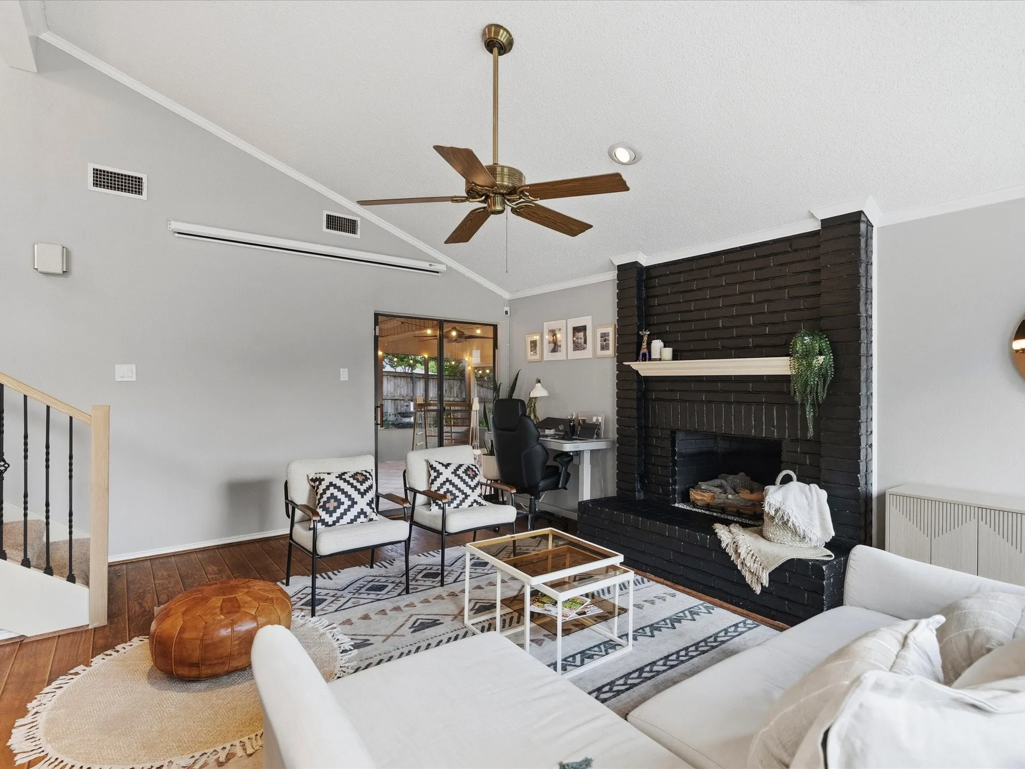 Vaulted ceiling living space featuring a dark brick fireplace with a mantle, wood-finish flooring, a ceiling fan, and black-framed glass patio doors