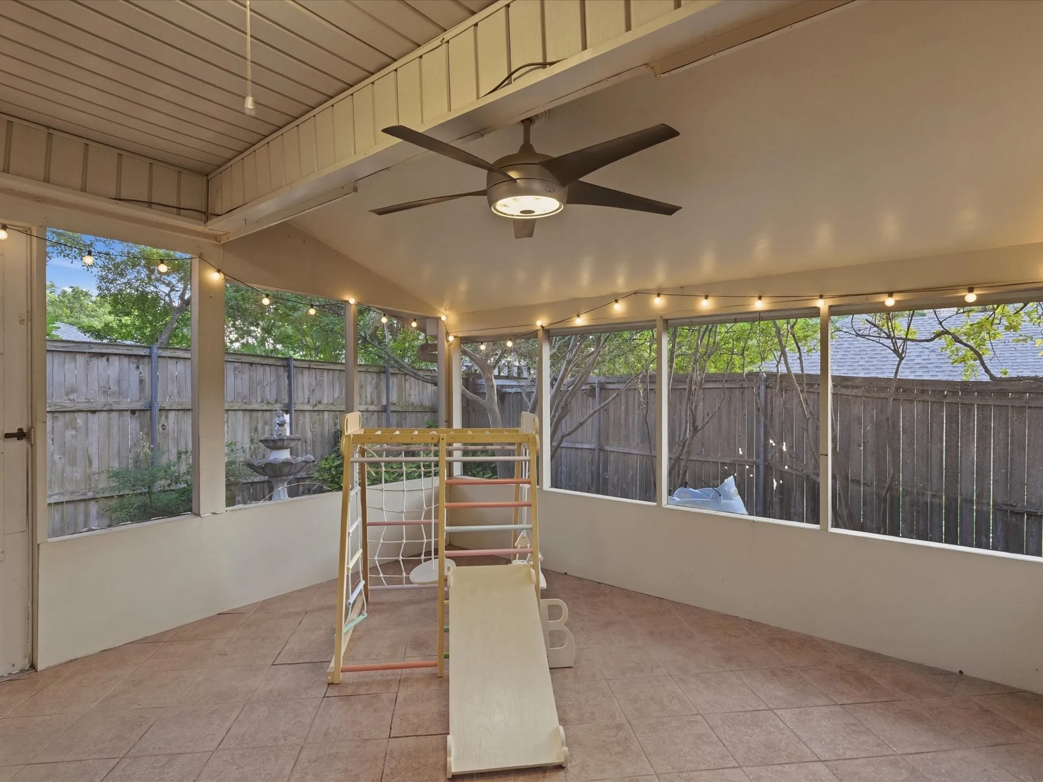 Screened porch featuring a ceiling fan, string lighting, tiled flooring, and a stone fountain