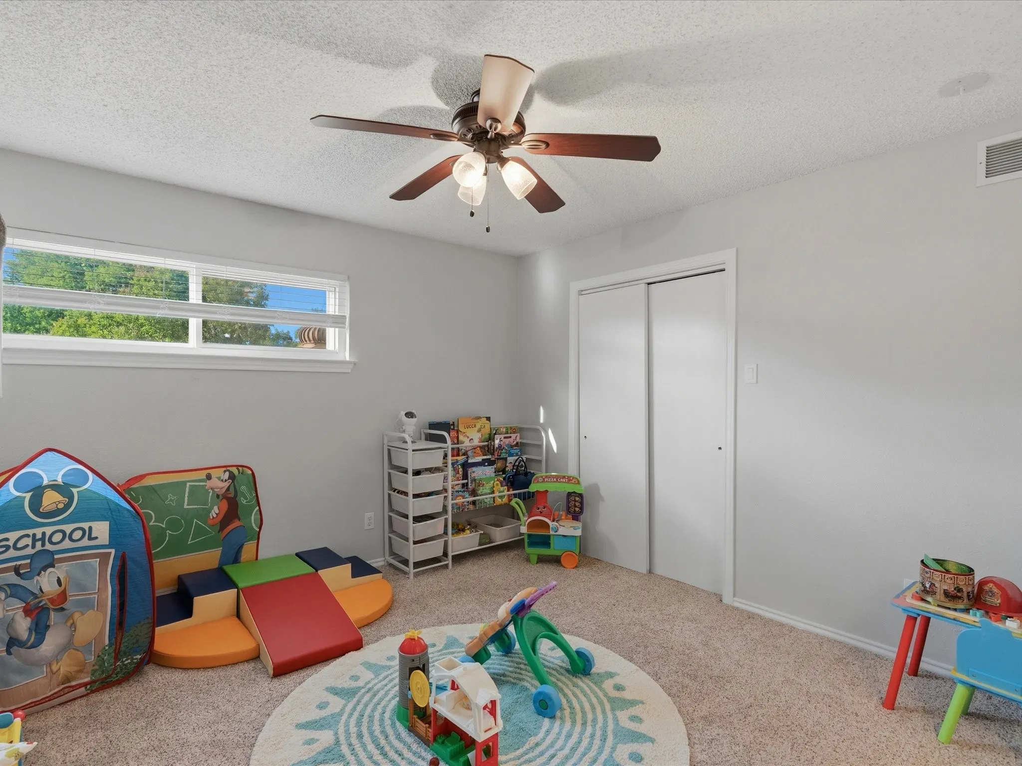 Carpeted room featuring a ceiling fan with light fixture, horizontal window, and sliding closet doors