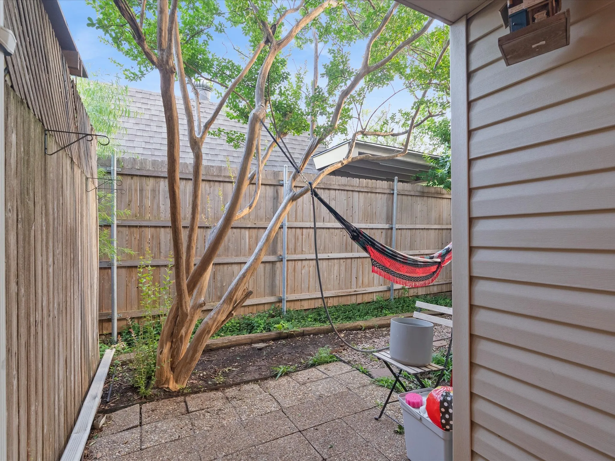 Private outdoor area featuring a mature tree, stone patio pavers, wood fencing, and neutral-toned siding