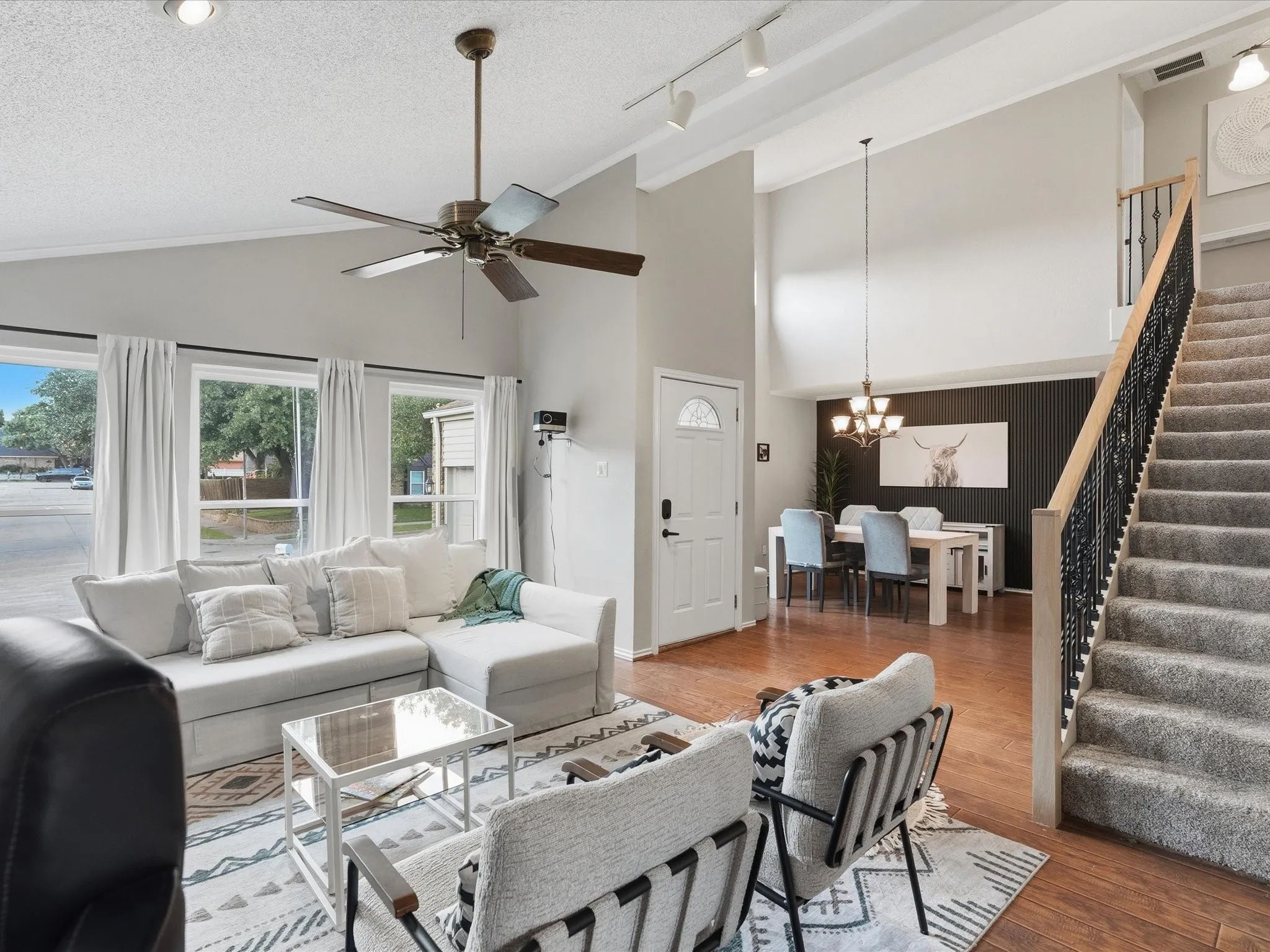 Spacious living area with vaulted ceilings, wood-finish flooring, and ample natural light from multiple windows
