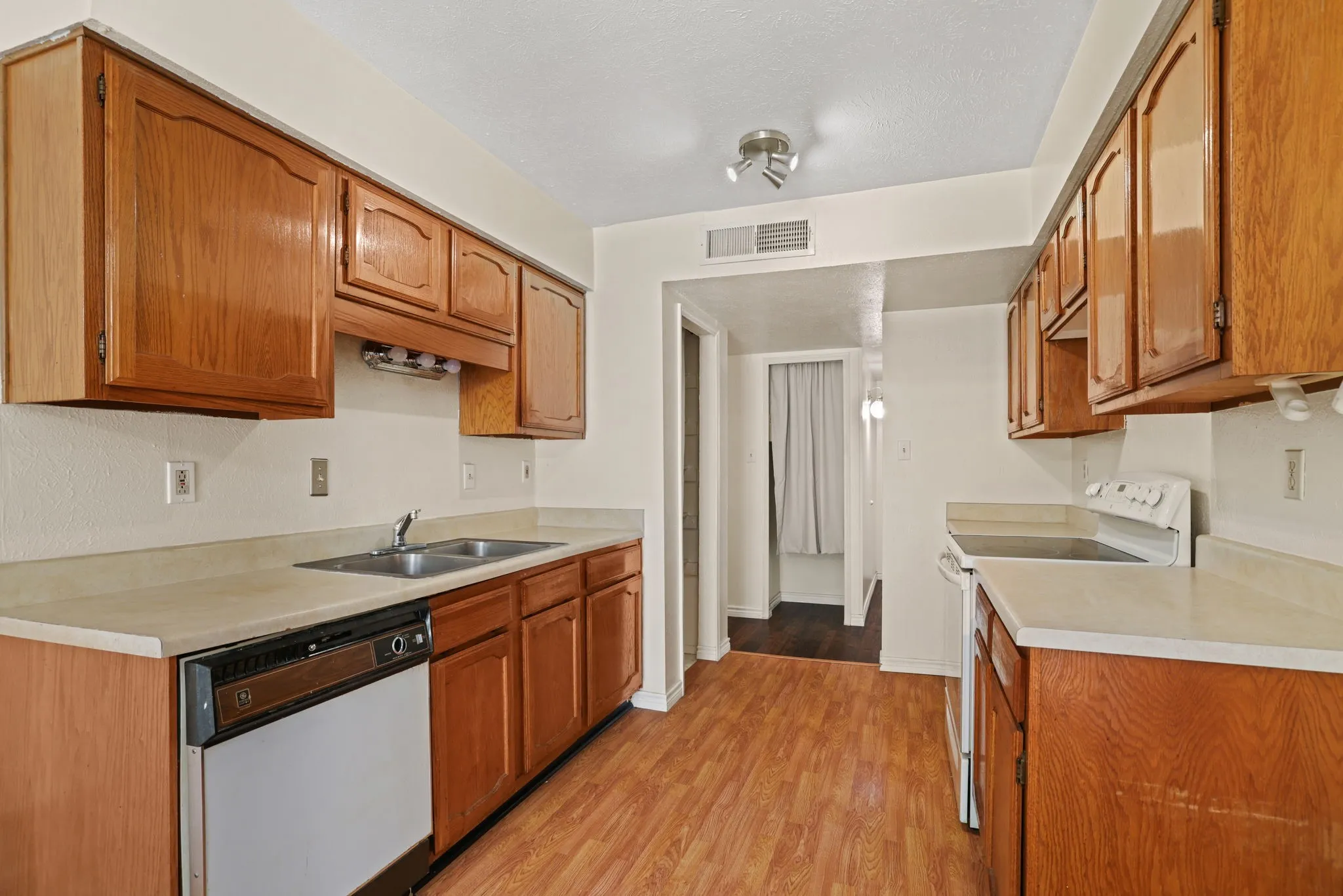 Kitchen featuring wood-finish flooring, wood cabinetry, light countertops, a double basin stainless steel sink, and a built-in dishwasher