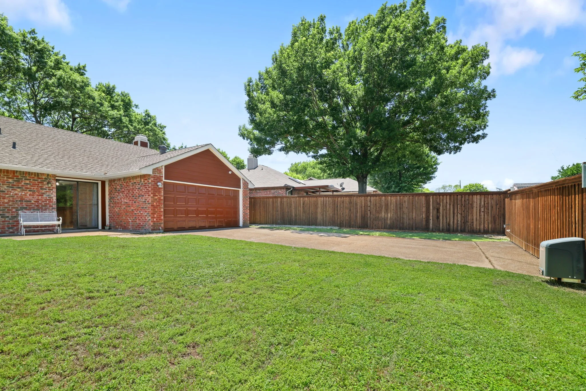 Brick exterior featuring an attached two-car garage with a paneled door, a sliding glass door, a large grassy area, and a wood privacy fence