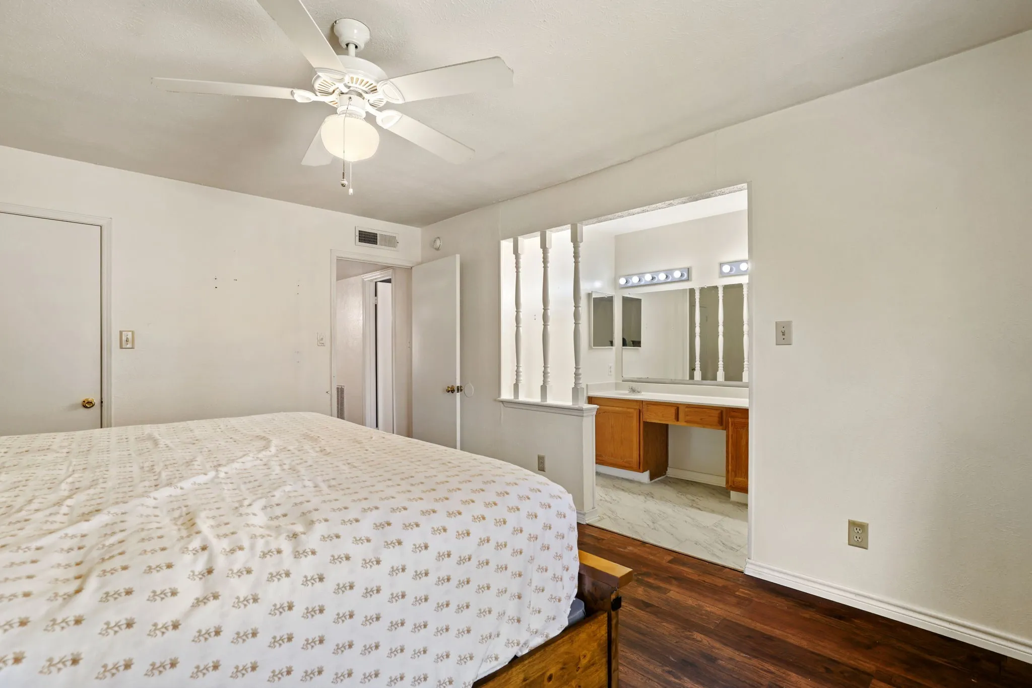 Bedroom featuring wood-finish flooring, a ceiling fan with integrated lighting, and direct access to a vanity area with a built-in wooden vanity