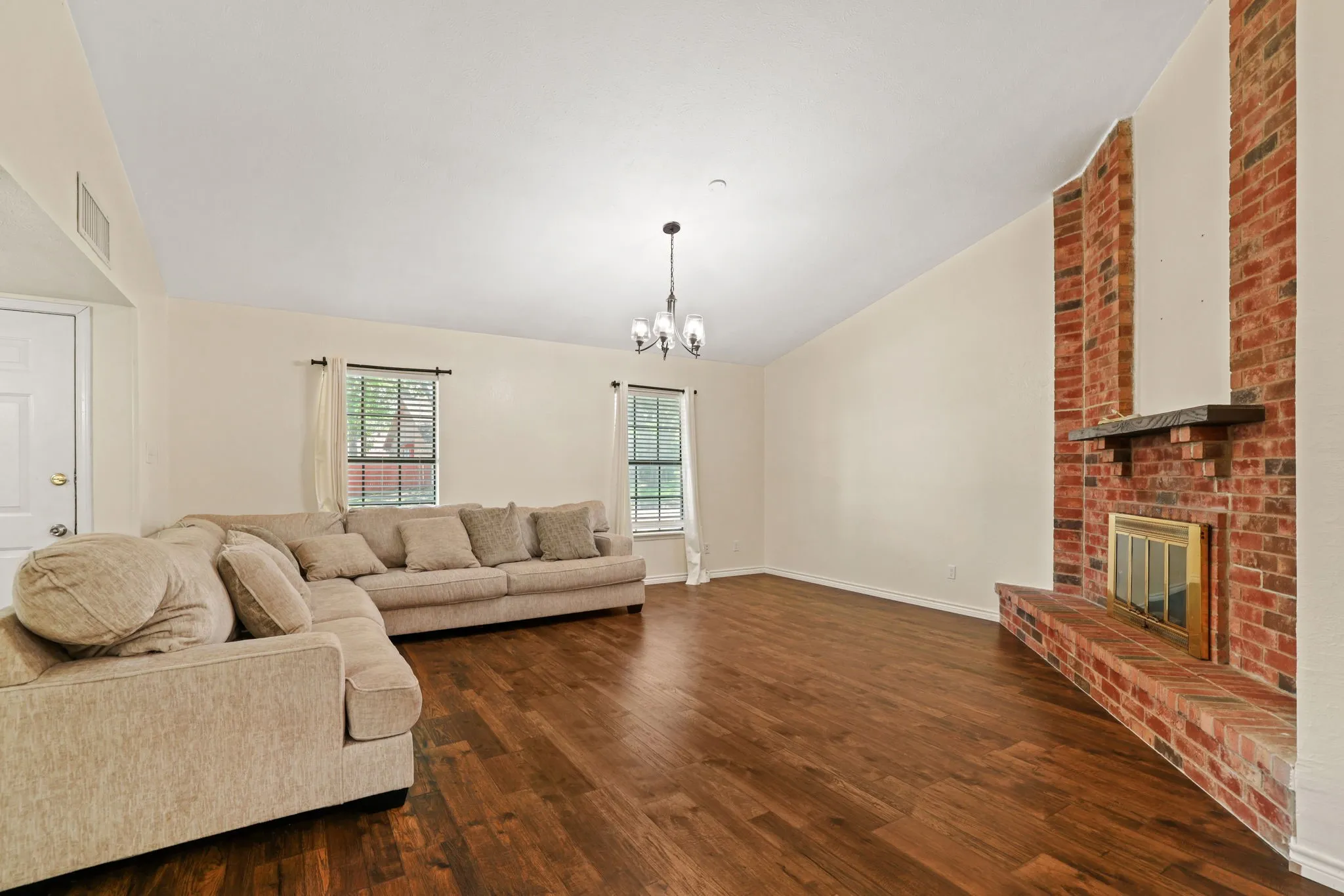 Spacious living area featuring a prominent brick fireplace with a dark wood mantel, high vaulted ceilings, and rich wood-finish flooring