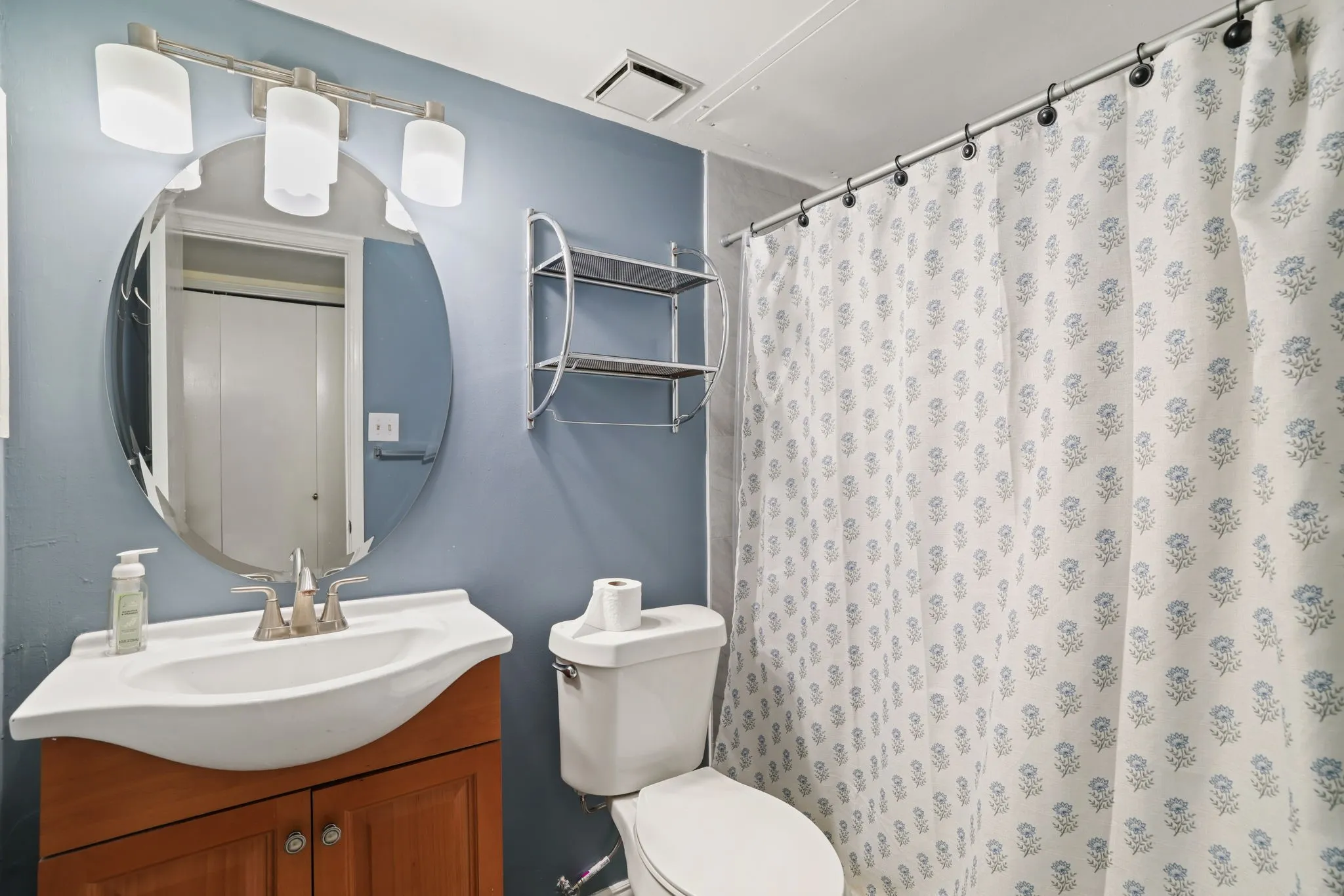 Bathroom featuring a wood-finish vanity with an integrated white sink, a circular mirror, and a three-light vanity fixture