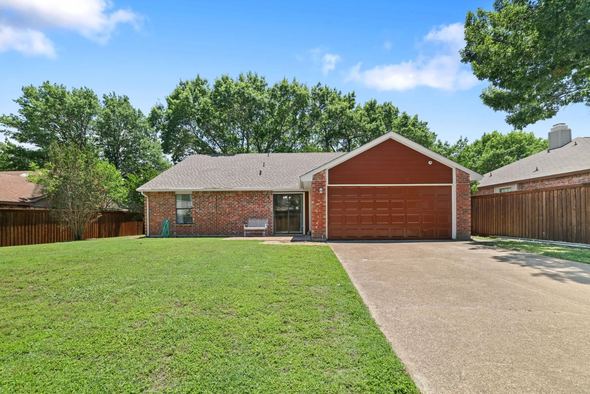Brick exterior featuring a two-car garage with a wood-finish door, a concrete driveway, and a front lawn