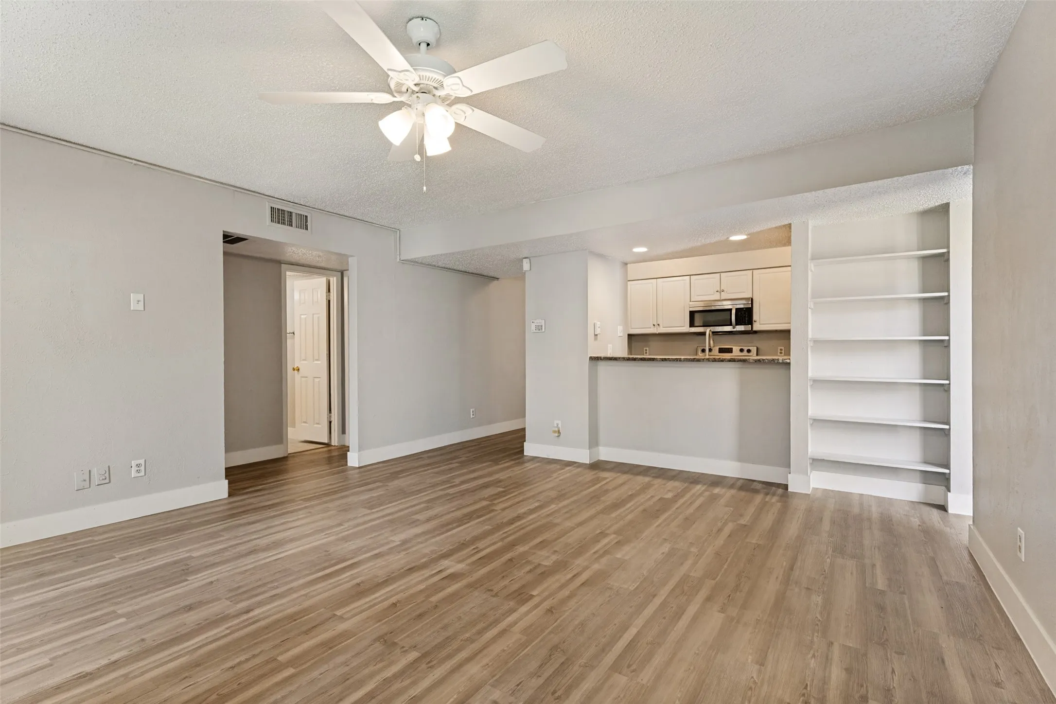 Open-concept living area with wood-finish flooring, a ceiling fan, and built-in shelving