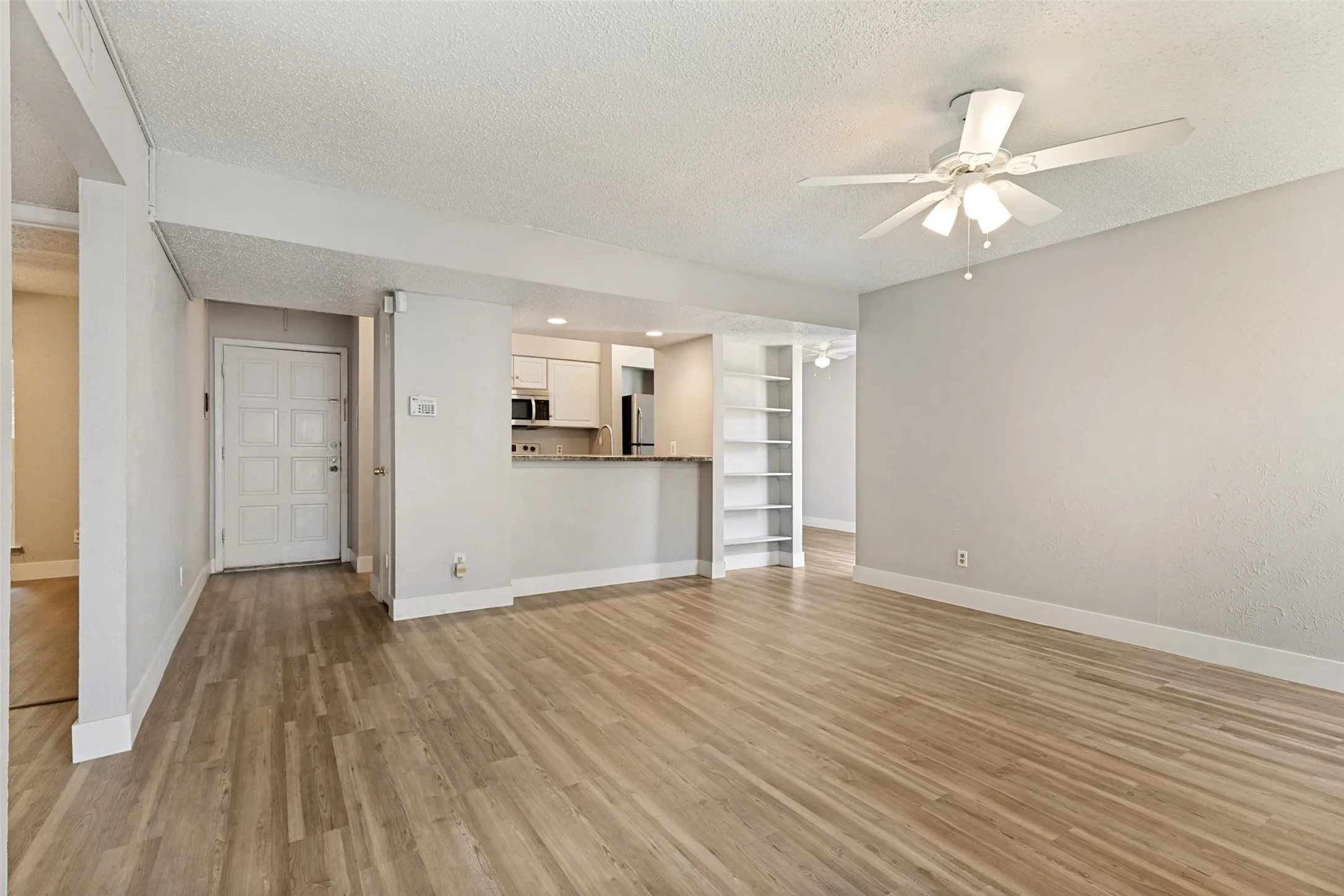 Spacious living area featuring wood-finish flooring, a ceiling fan with integrated lighting, and a built-in shelving unit