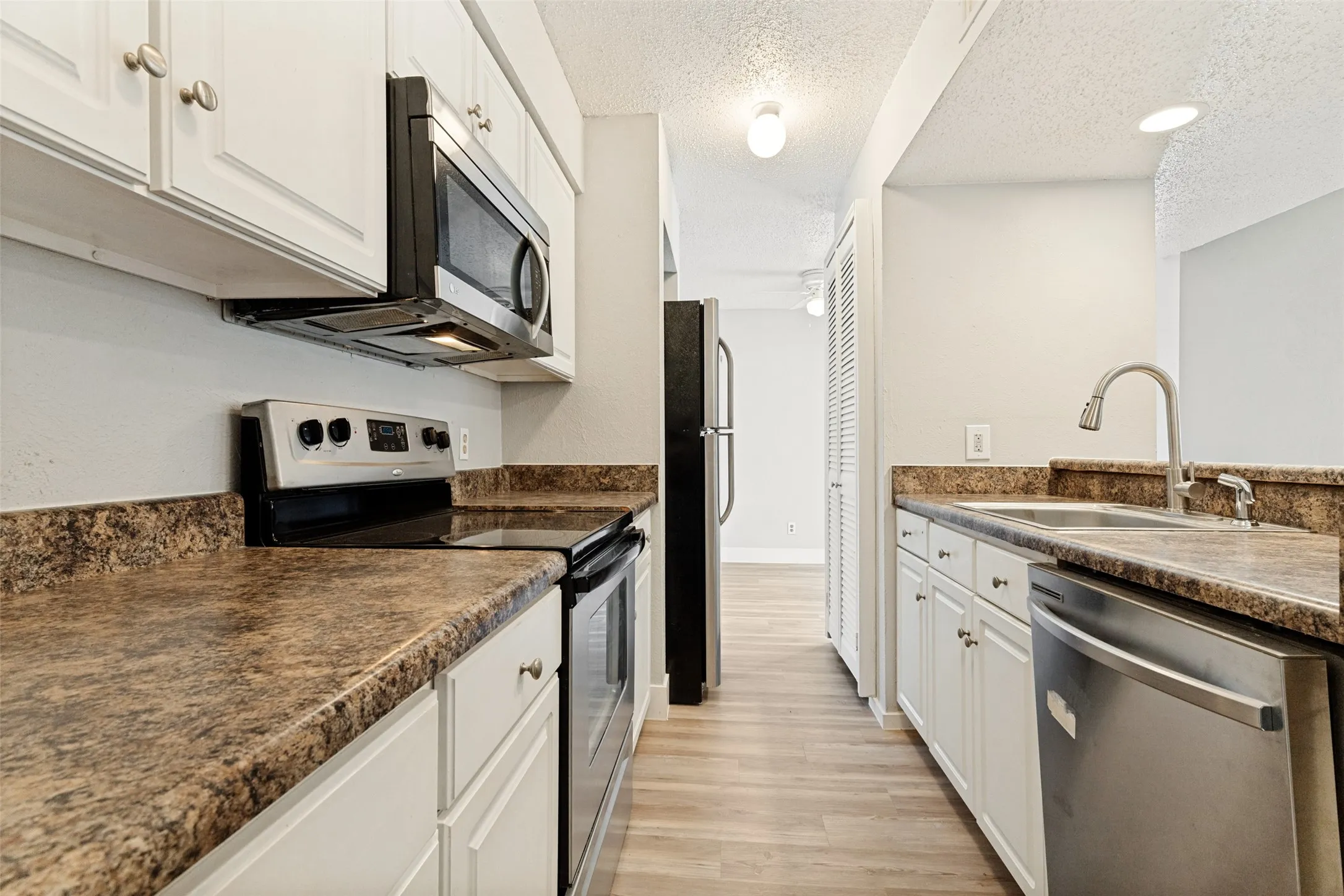 Kitchen featuring white cabinetry, speckled countertops, stainless steel appliances, and wood-finish flooring