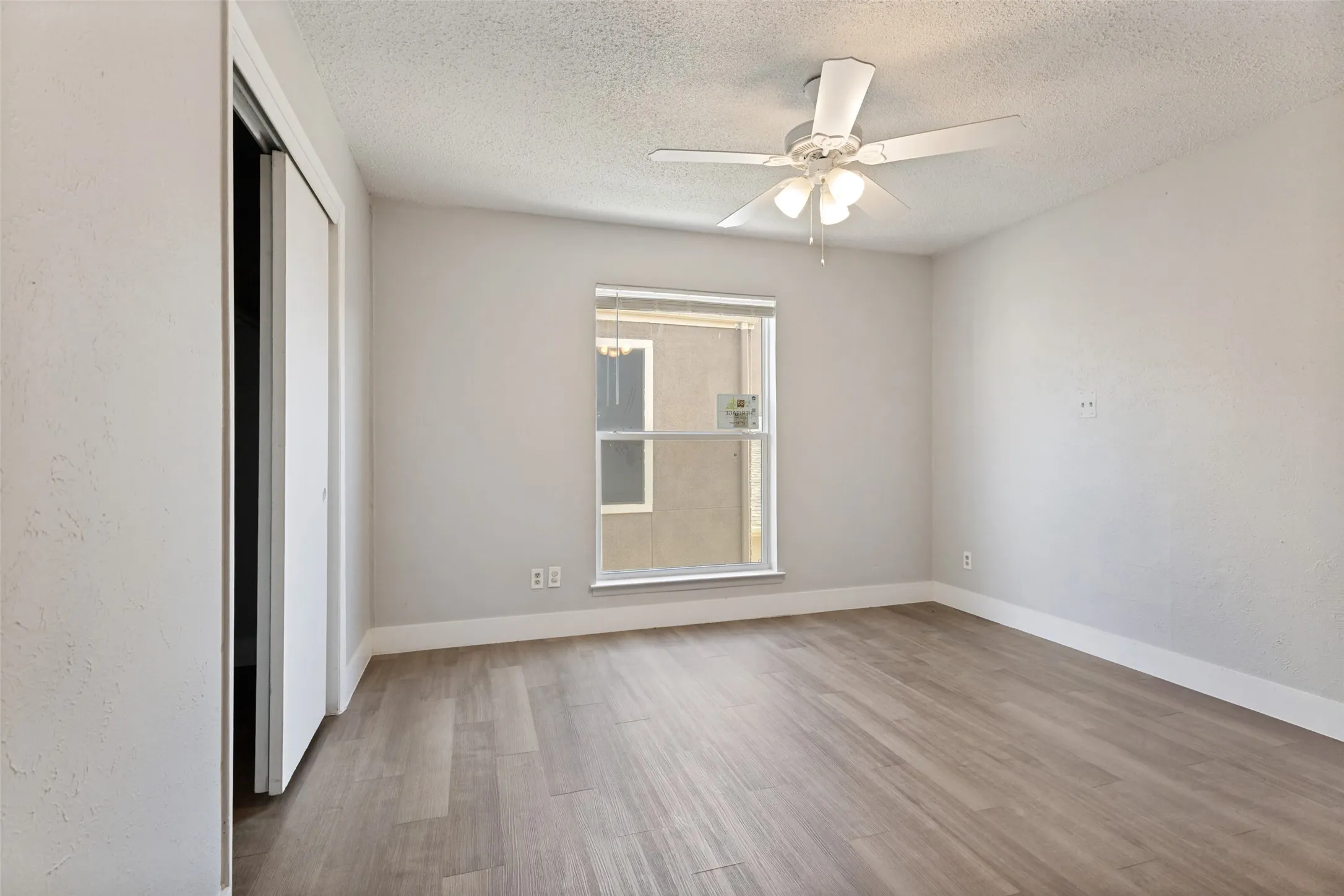 Room featuring wood-finish flooring, a ceiling fan with integrated lighting, a double-hung window, and sliding closet doors