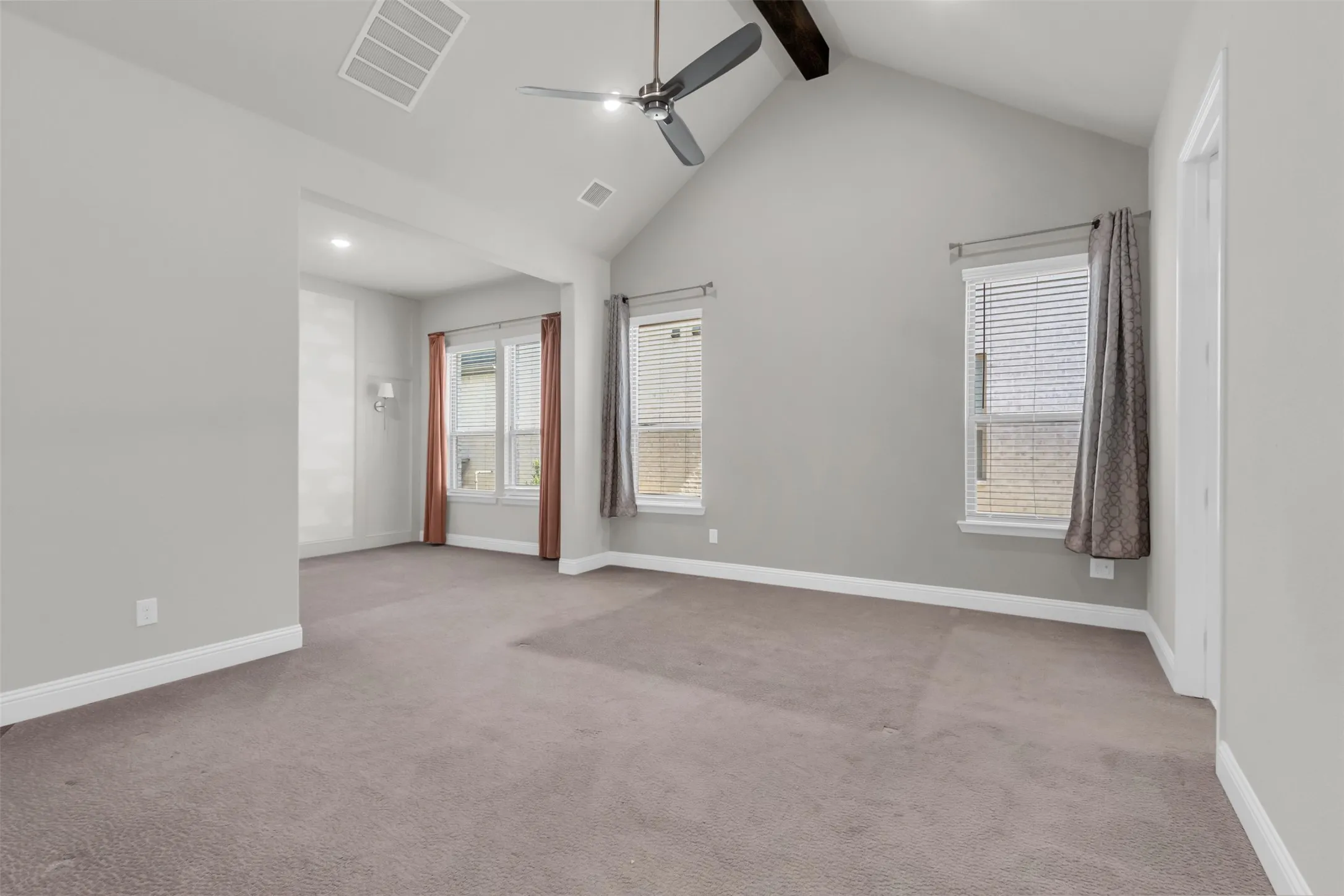 Carpeted spare room with ceiling fan and vaulted ceiling with beams