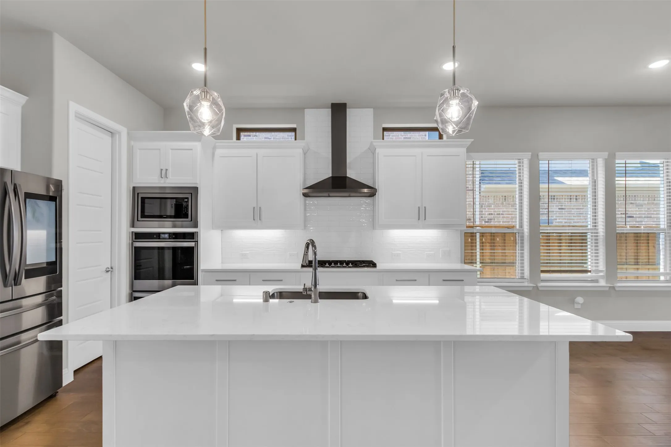Kitchen with appliances with stainless steel finishes, hardwood / wood-style flooring, wall chimney exhaust hood, and decorative light fixtures