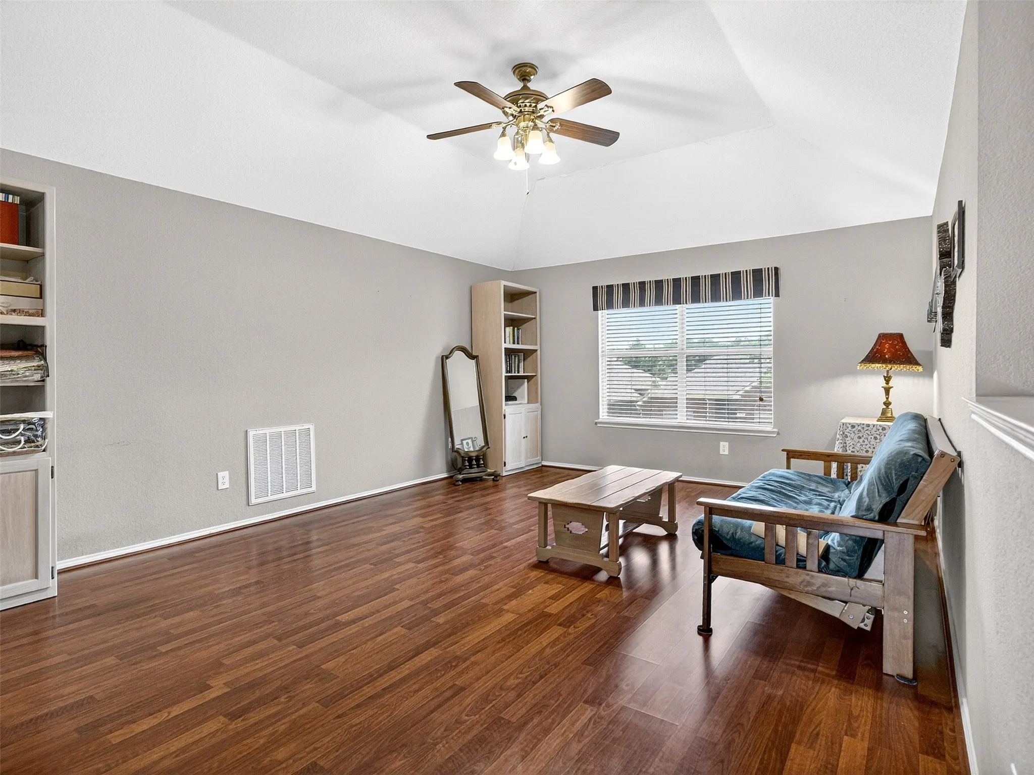Spacious room featuring wood-finish flooring, vaulted ceiling, and a ceiling fan with light fixture