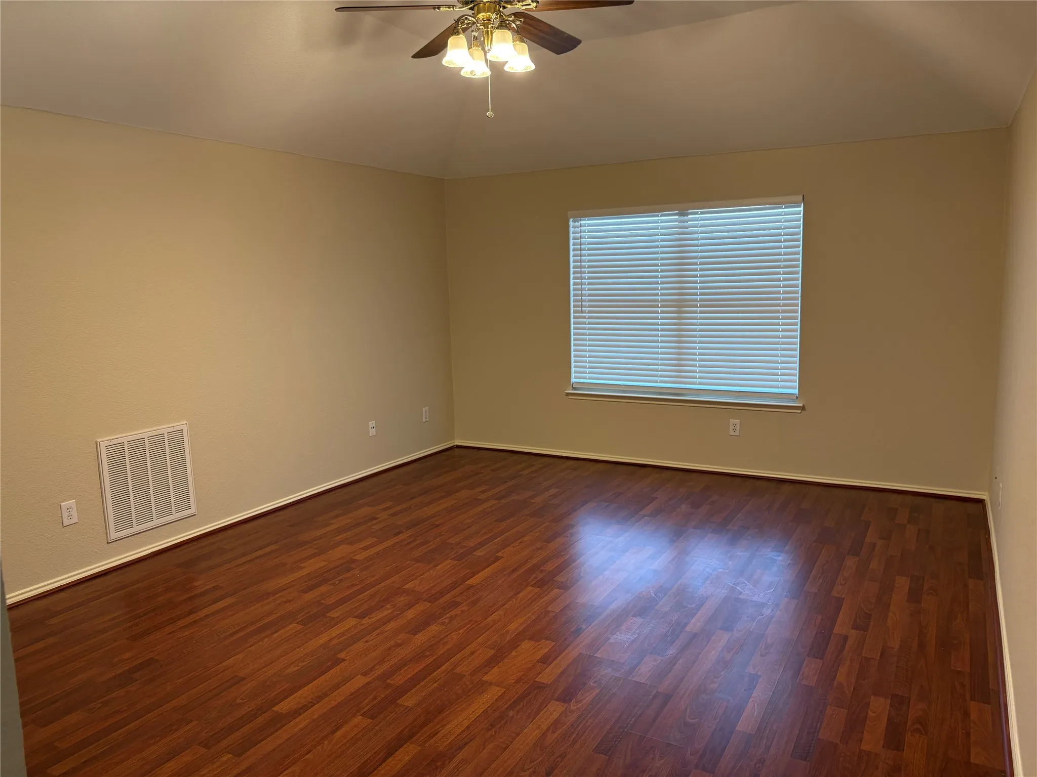 Spacious room featuring rich wood-finish flooring, neutral wall tones, and a ceiling fan with integrated lighting