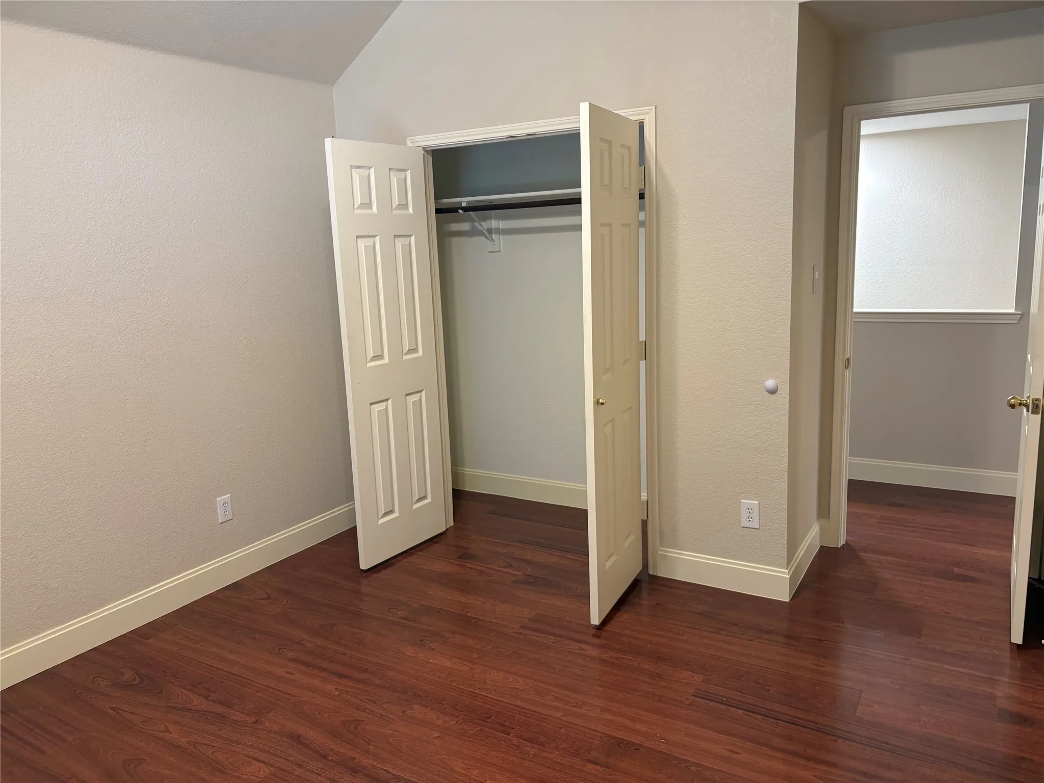Room featuring rich wood-finish flooring, light-toned walls, white baseboards, and a vaulted ceiling