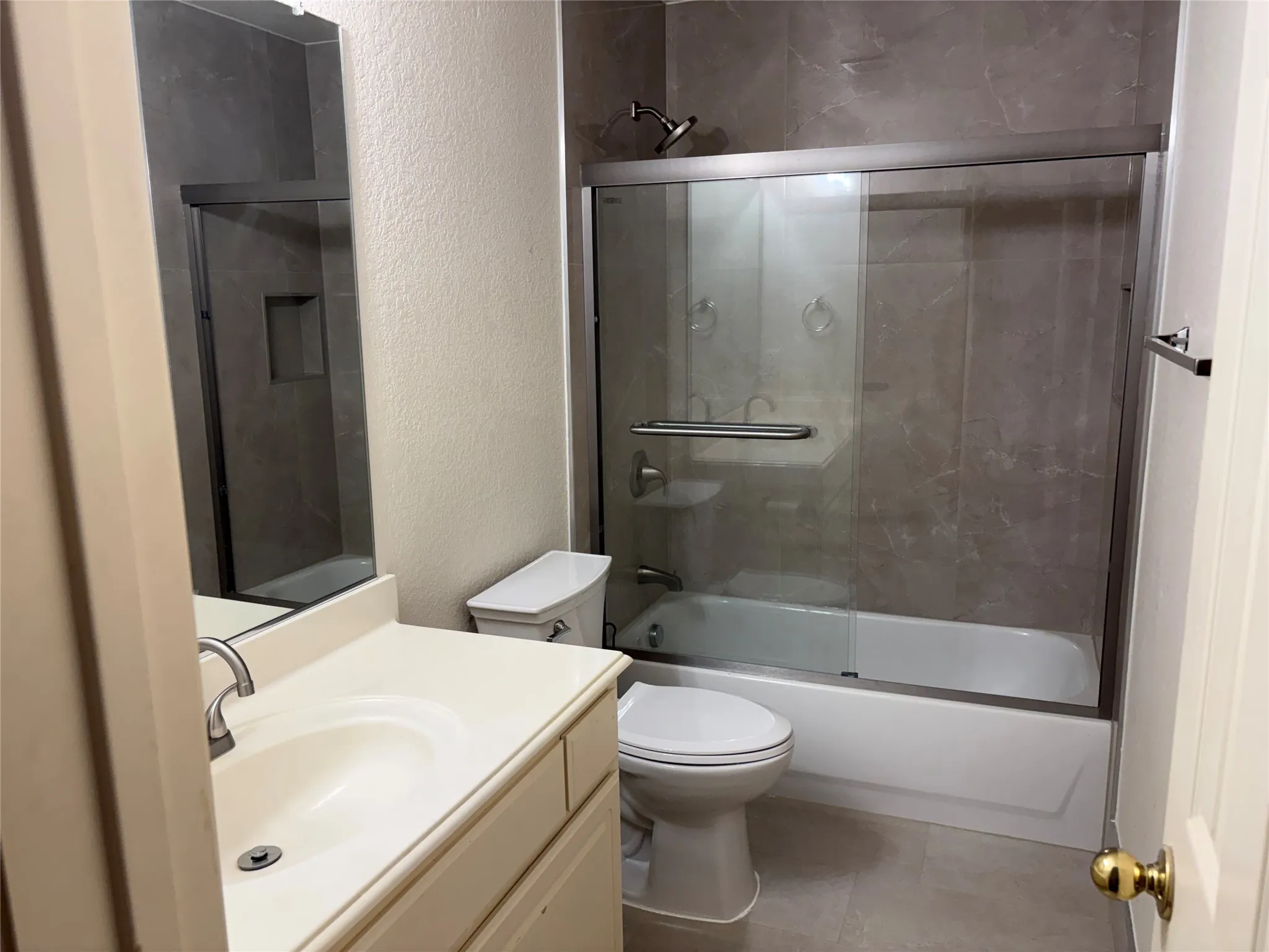 Bathroom featuring a tub/shower combination with a sliding glass enclosure, a built-in shower niche, and full-height tiled walls