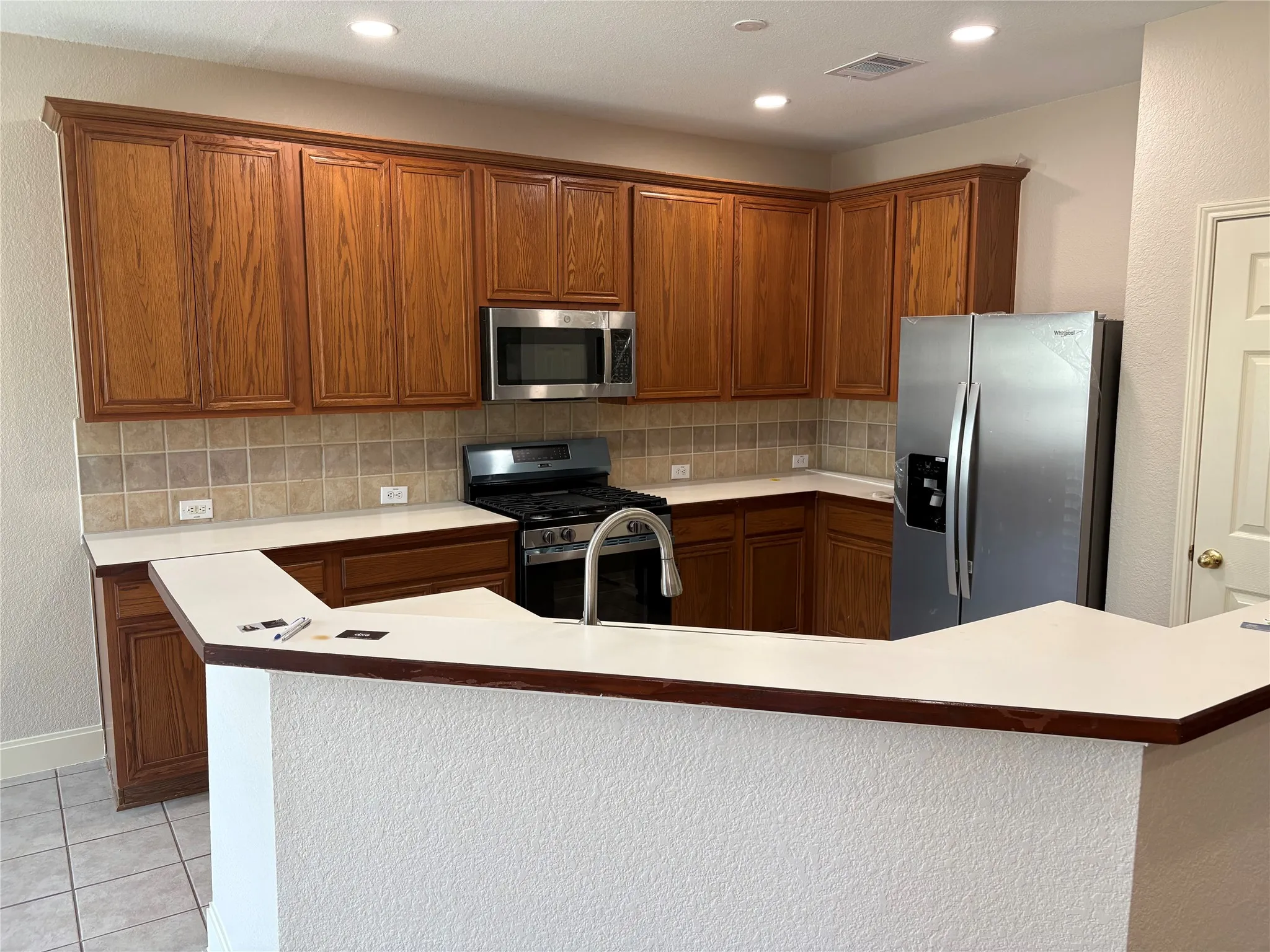 U-shaped kitchen featuring wood cabinetry, light-toned countertops, and a tile backsplash