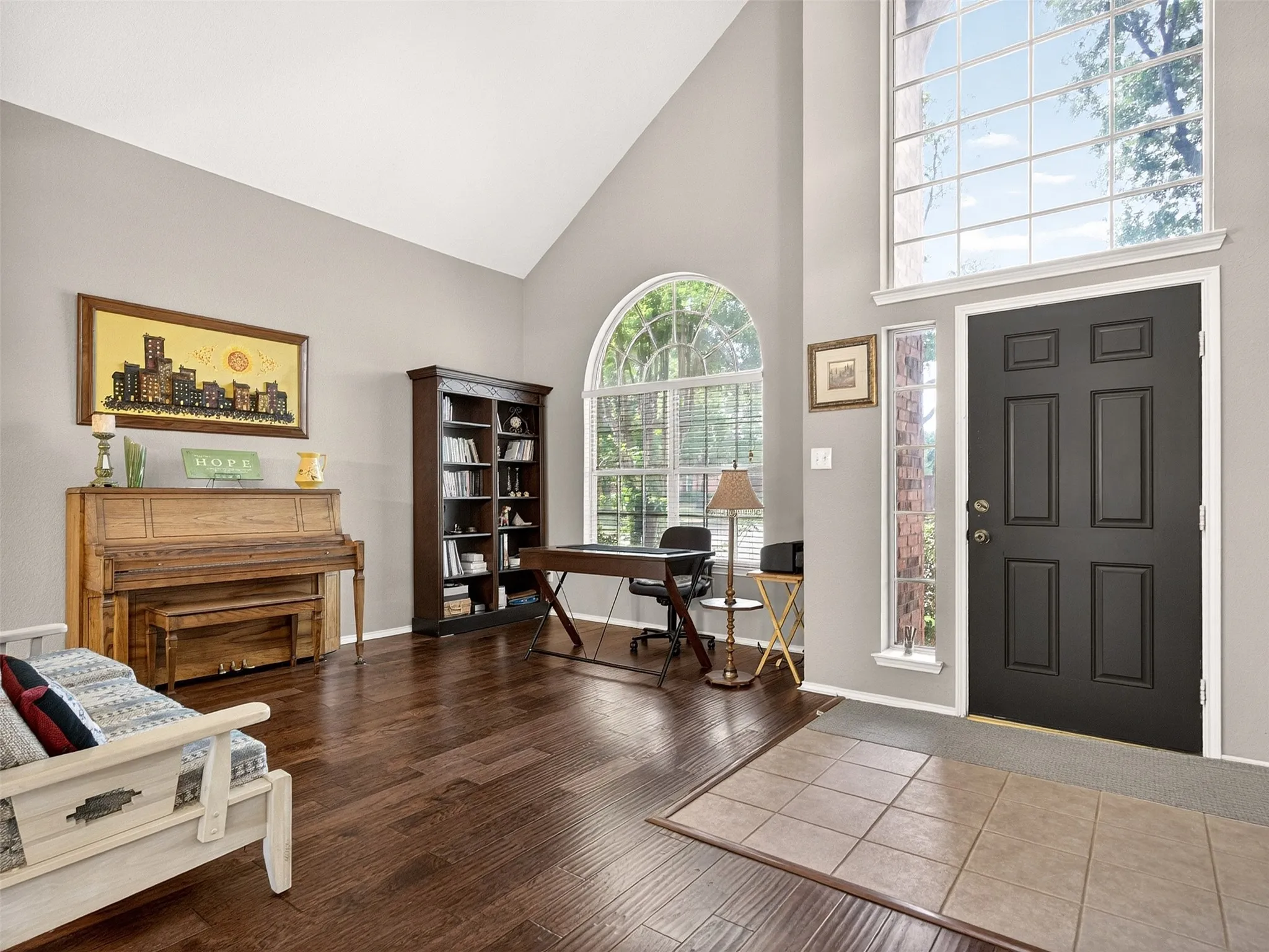 Two-story foyer featuring a dark-paneled entry door, arched transom window, and wood-finish flooring