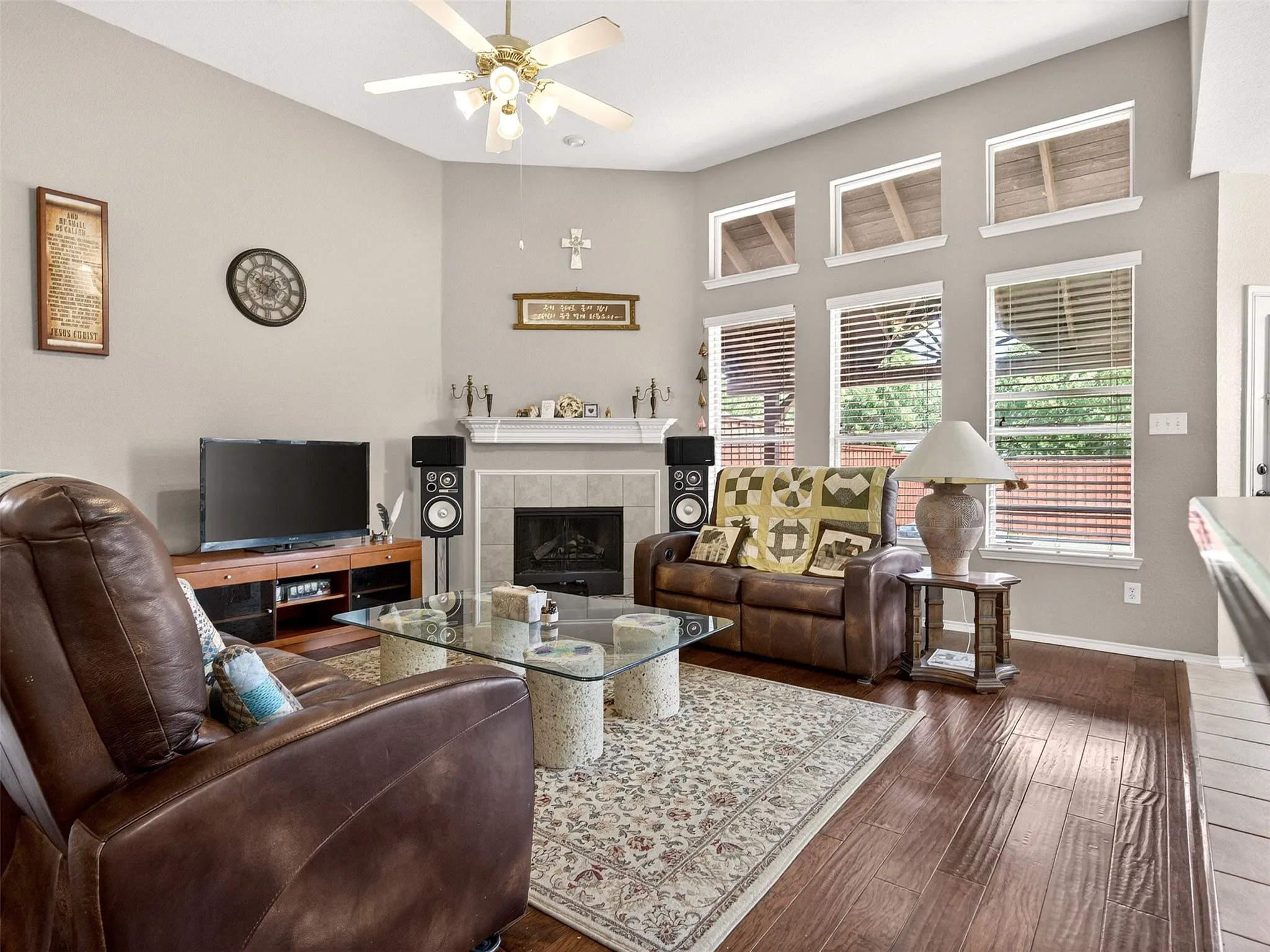 Living area featuring vaulted ceilings, a ceiling fan, a fireplace with a mantel and tile surround, and wood-finish flooring