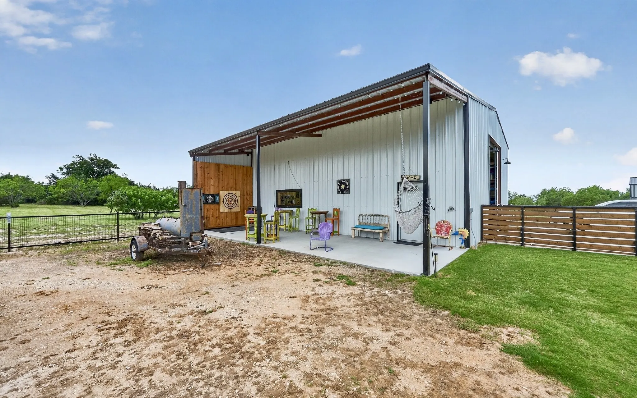Metal building with an integrated covered patio, exposed structural beams, wood-plank accent wall, and a horizontal slat fence