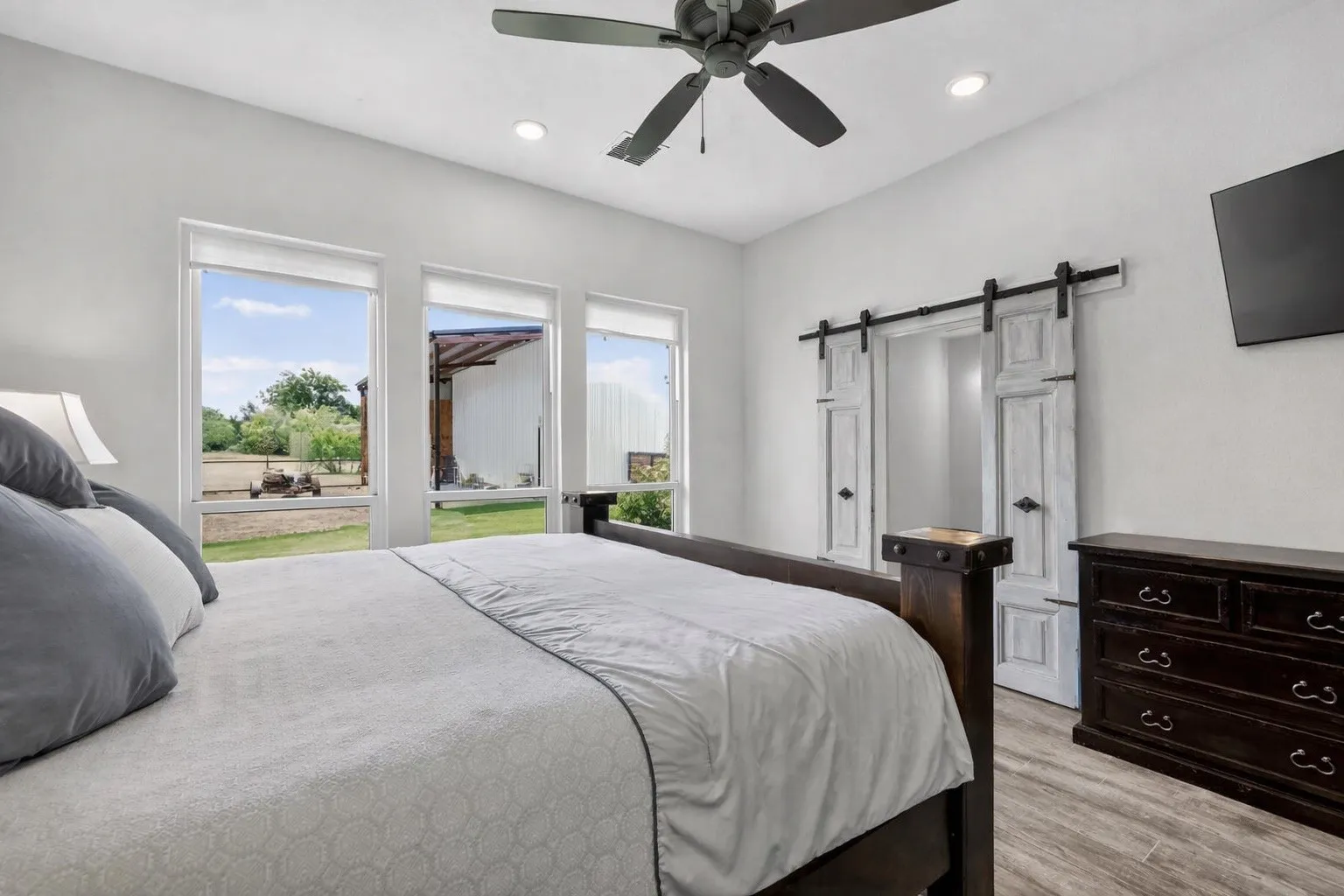 Bright interior featuring three large windows, wood-finish flooring, a ceiling fan, recessed lighting, and a barn door