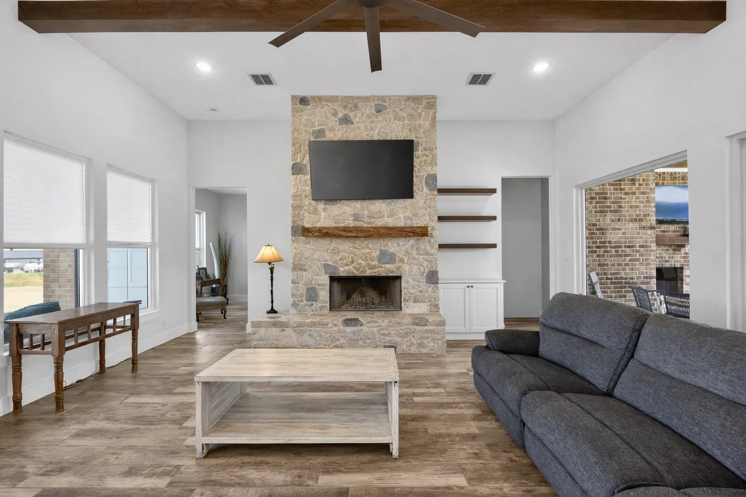 Spacious living area featuring a floor-to-ceiling stone fireplace, wood-finish flooring, exposed ceiling beams, recessed lighting, and built-in shelving with cabinetry