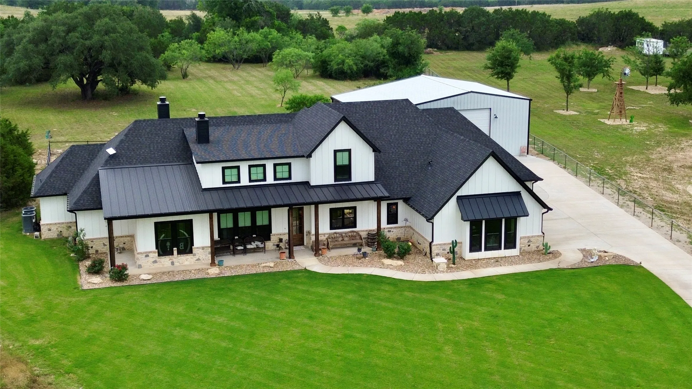 Modern farmhouse exterior featuring white siding, black-framed windows, a covered front porch, and stone accents