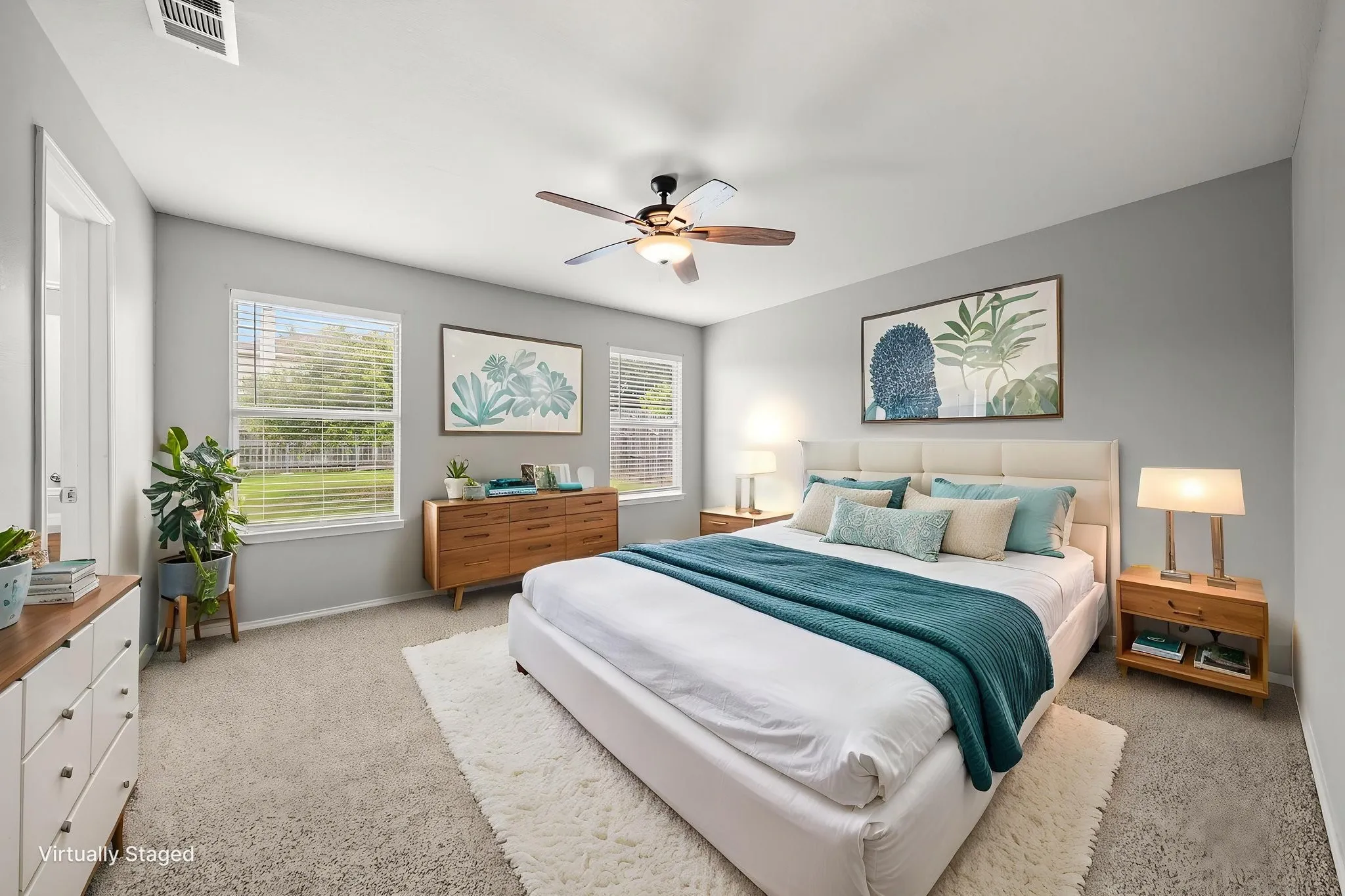 Spacious bedroom featuring light gray wall paint, neutral carpeting, multiple windows with blinds, and a ceiling fan with light fixture