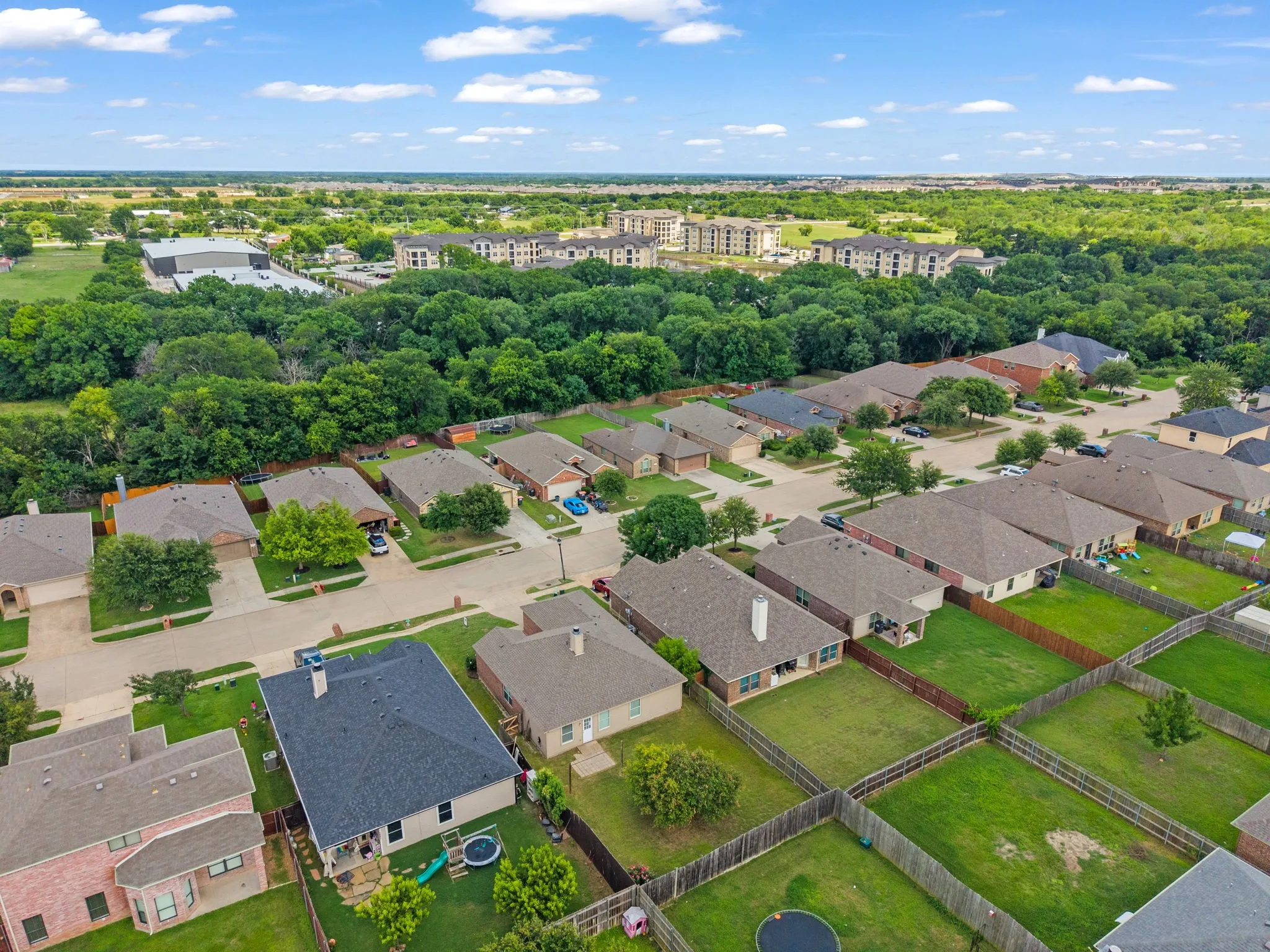 Aerial perspective showcasing a residential neighborhood with single-story homes, individual fenced backyards, paved streets, and abundant mature trees