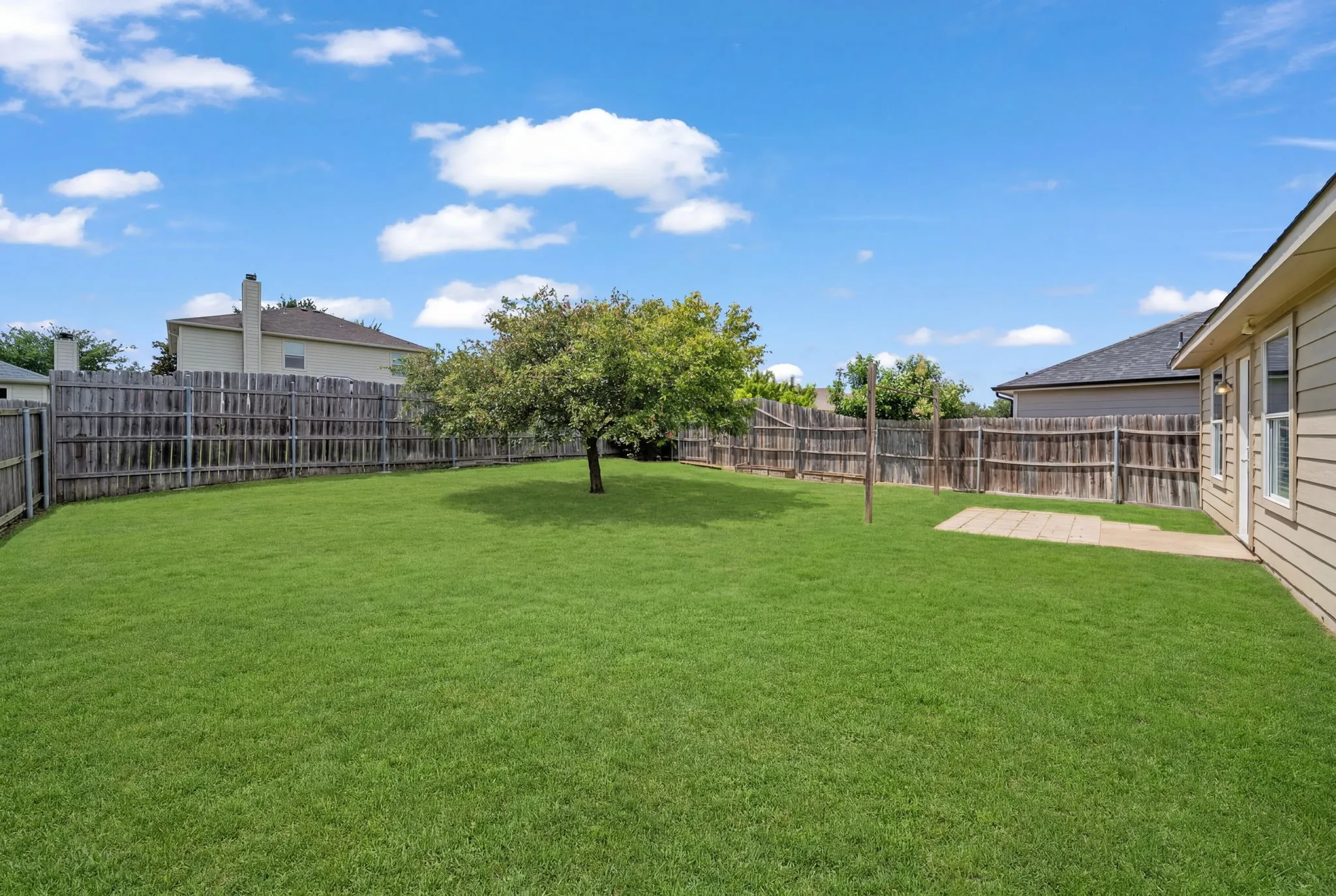 Expansive grassy yard featuring a mature tree, privacy fencing, and a concrete patio area