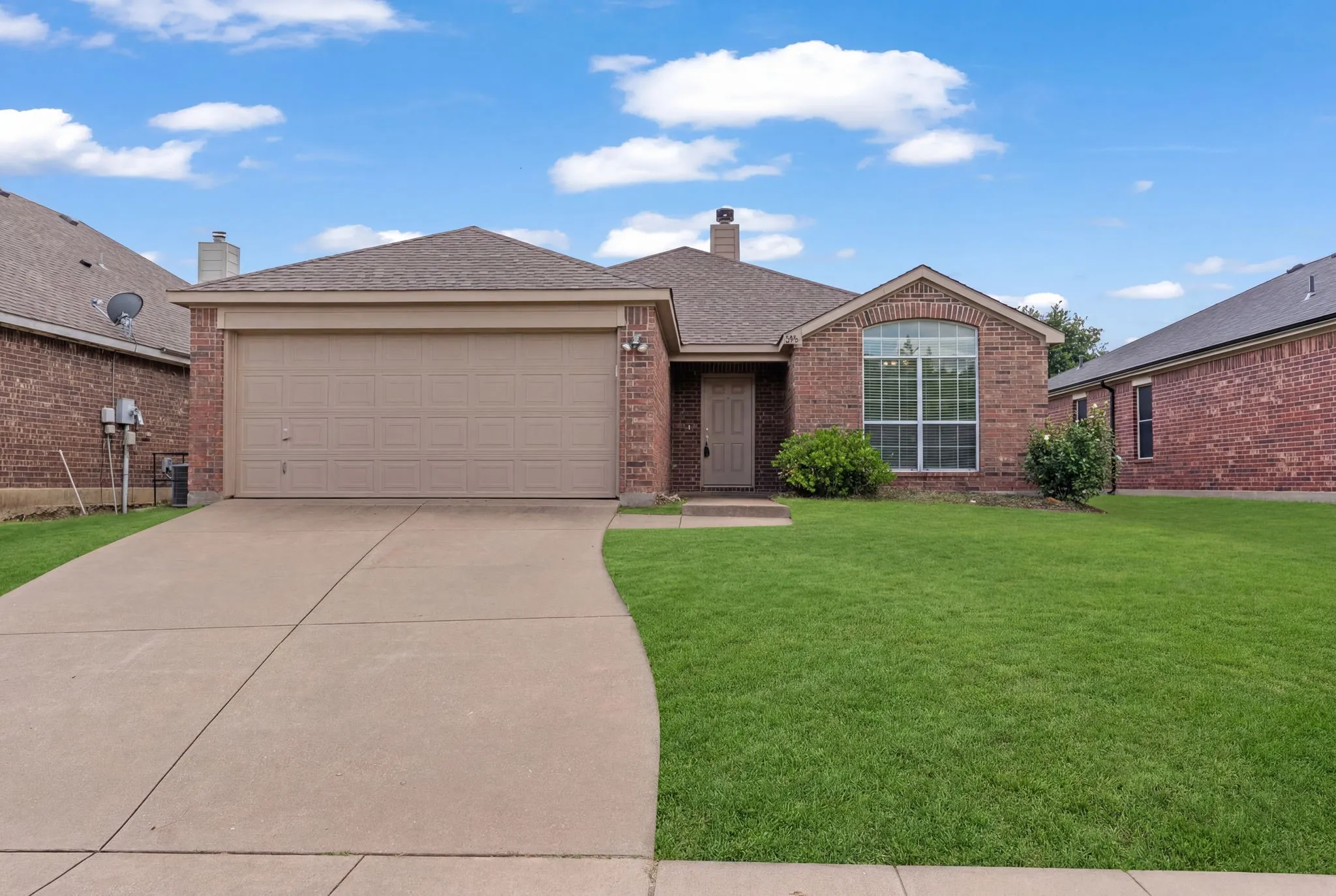 Traditional brick residence featuring an arched window, a two-car garage, and a concrete driveway