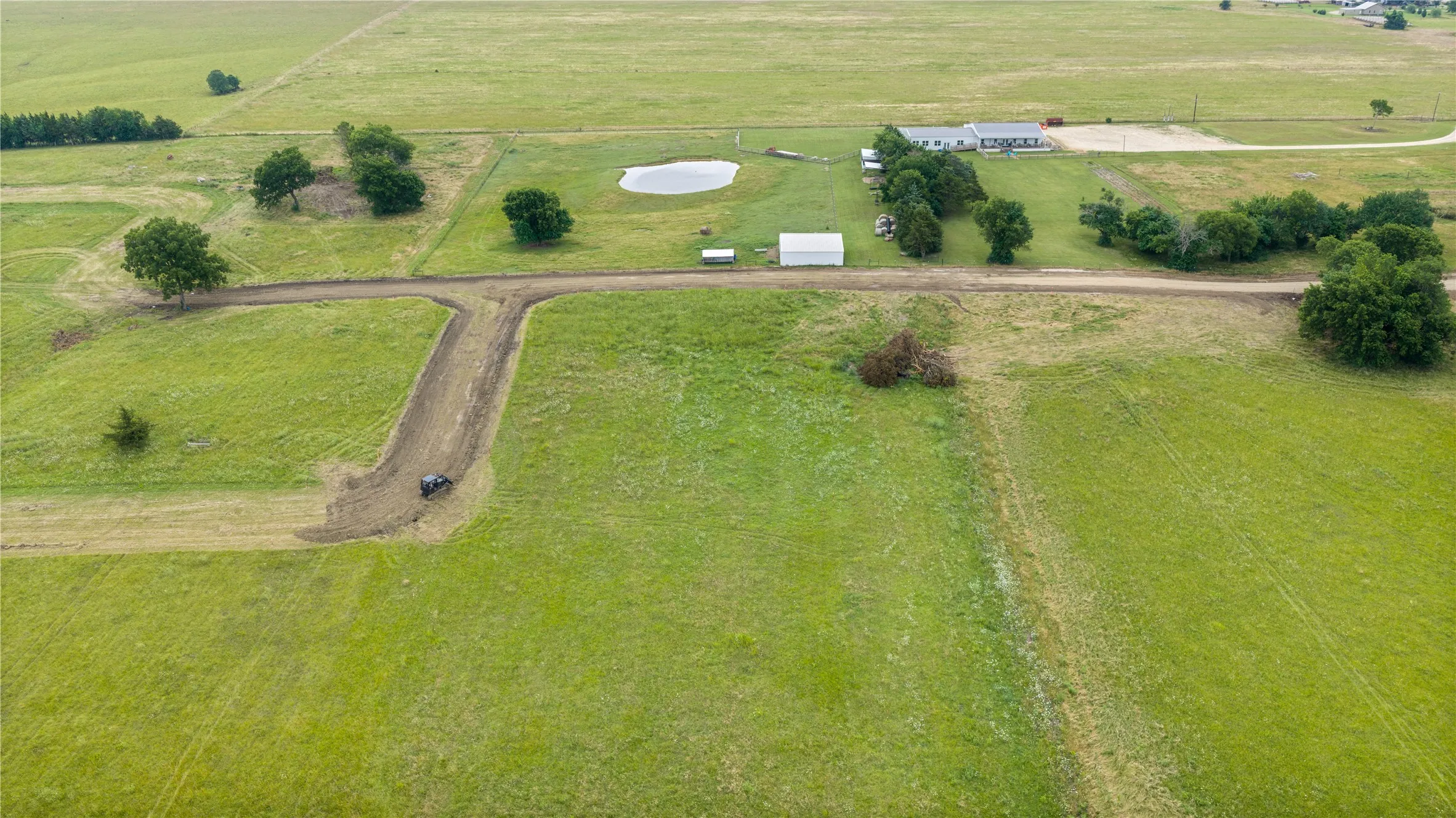 Expansive green acreage with a central pond and established trees