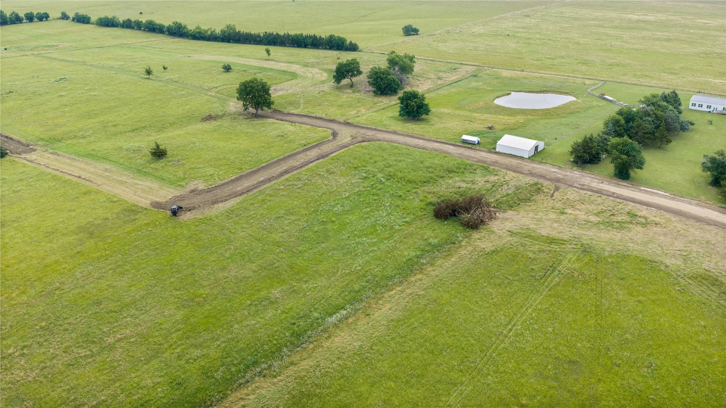 Expansive green acreage featuring a private pond, open fields, multiple mature trees, and a dirt access road