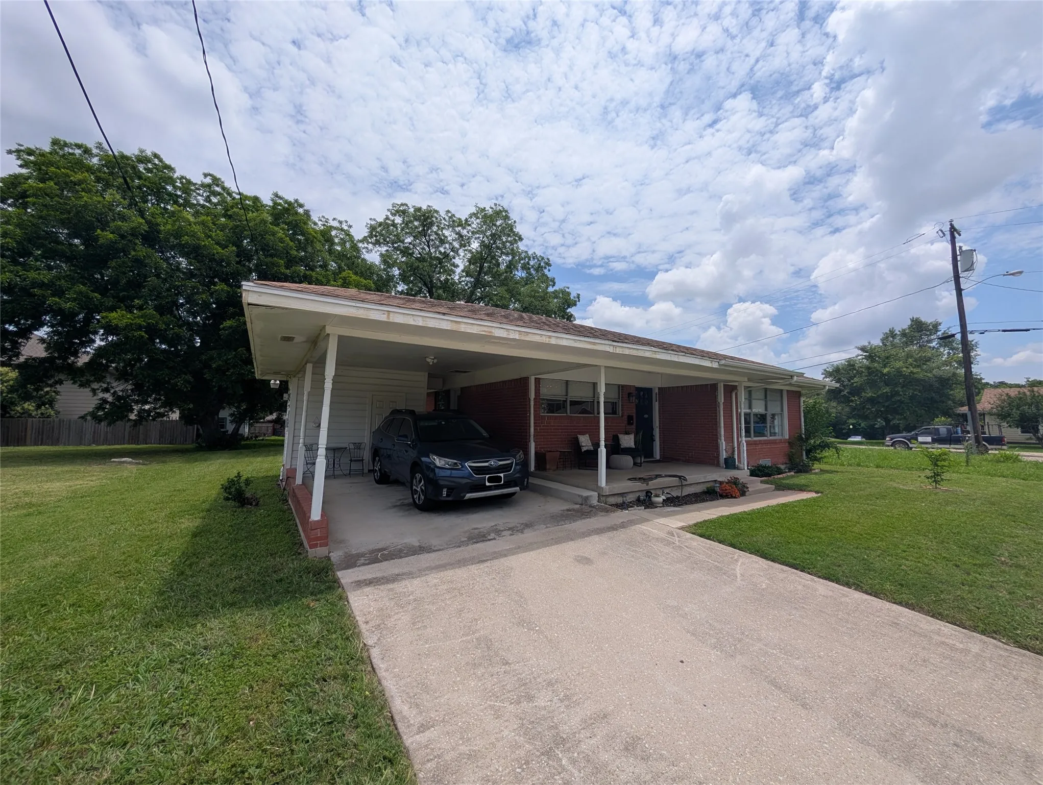 Brick exterior with a covered carport, concrete driveway, and front porch