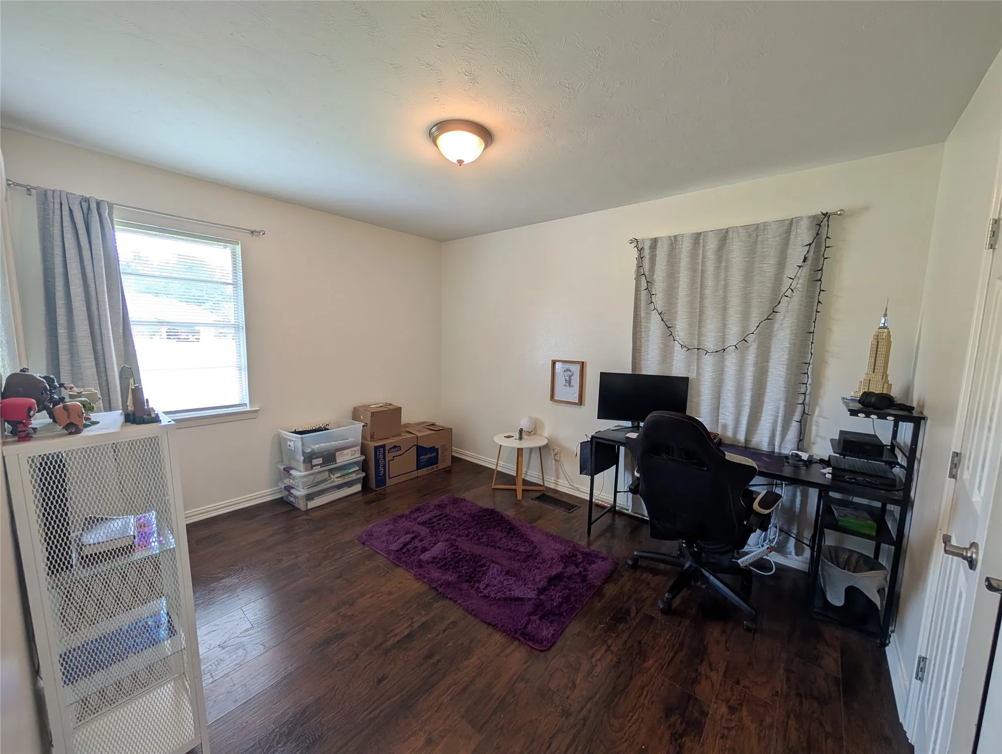 Spacious interior room with wood-finish flooring, white walls, and a ceiling-mounted light fixture