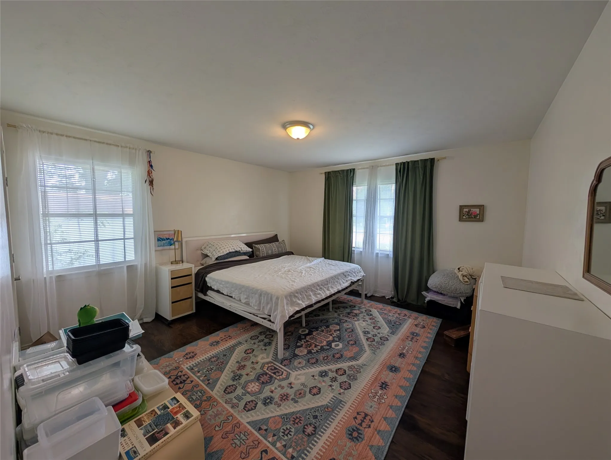 Spacious bedroom featuring dark wood-finish flooring, white walls, and a ceiling-mounted light fixture