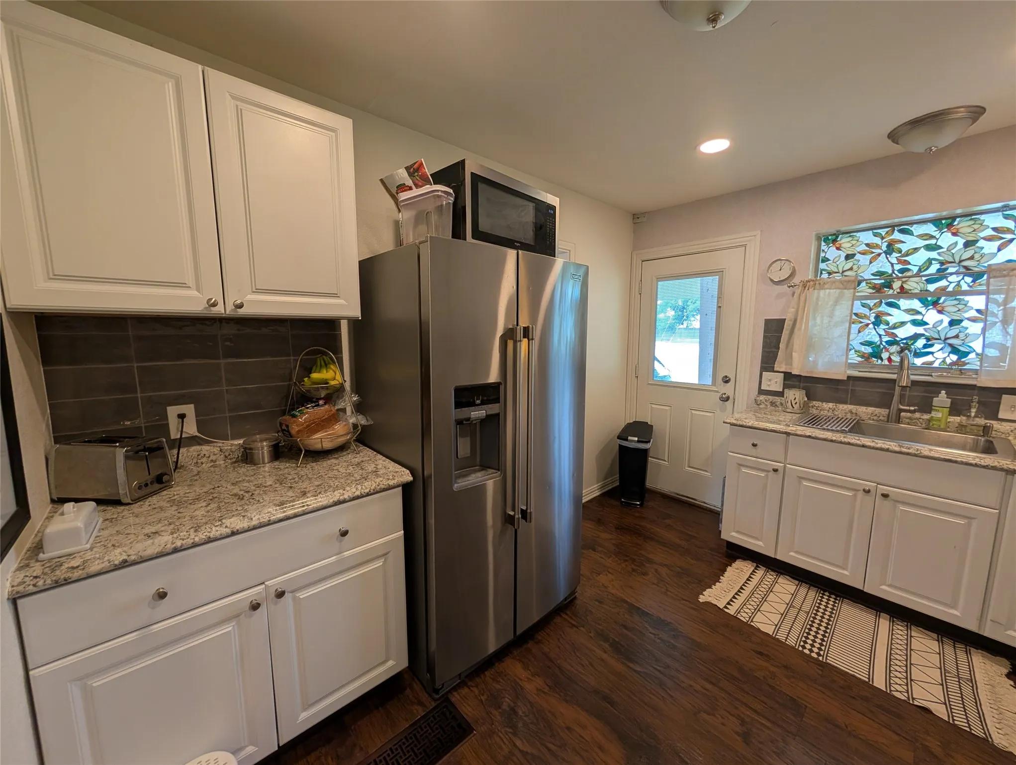 Kitchen featuring white shaker-style cabinetry, granite-look countertops, and a dark tile backsplash