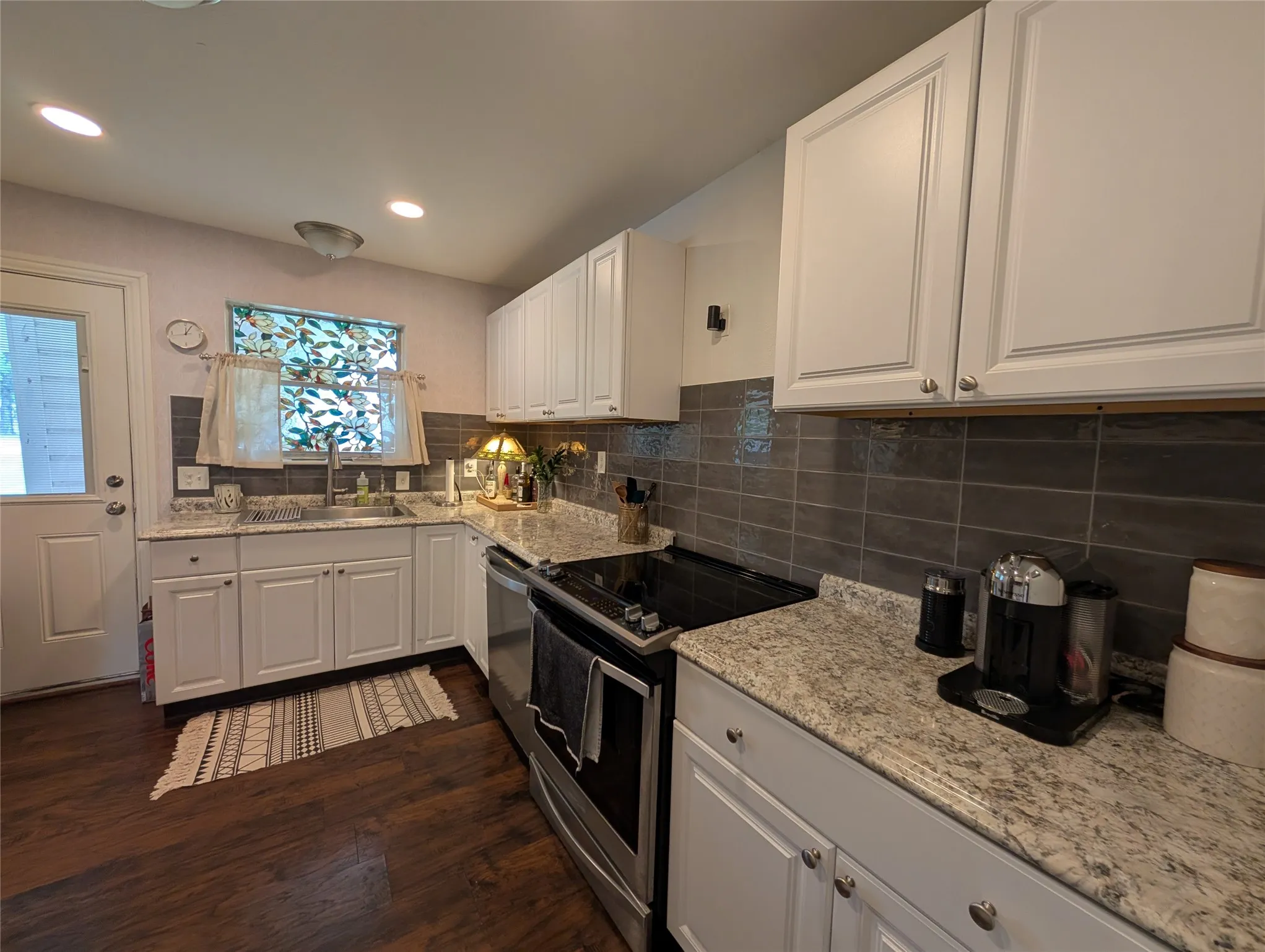 Kitchen featuring white cabinetry, light-toned countertops, a dark subway tile backsplash, stainless steel appliances, and dark wood-finish flooring