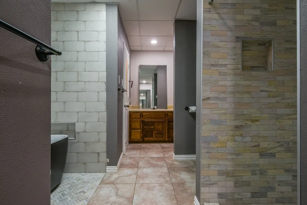 Walk-in shower featuring multi-toned horizontal tile, a built-in shower niche, and a contrasting white block-patterned wall