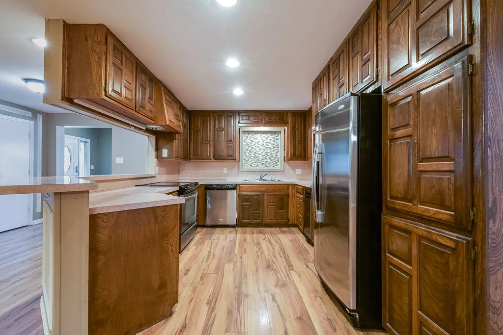 Kitchen featuring wood-finish flooring, abundant wood cabinetry, stainless steel appliances, and a pass-through opening.
