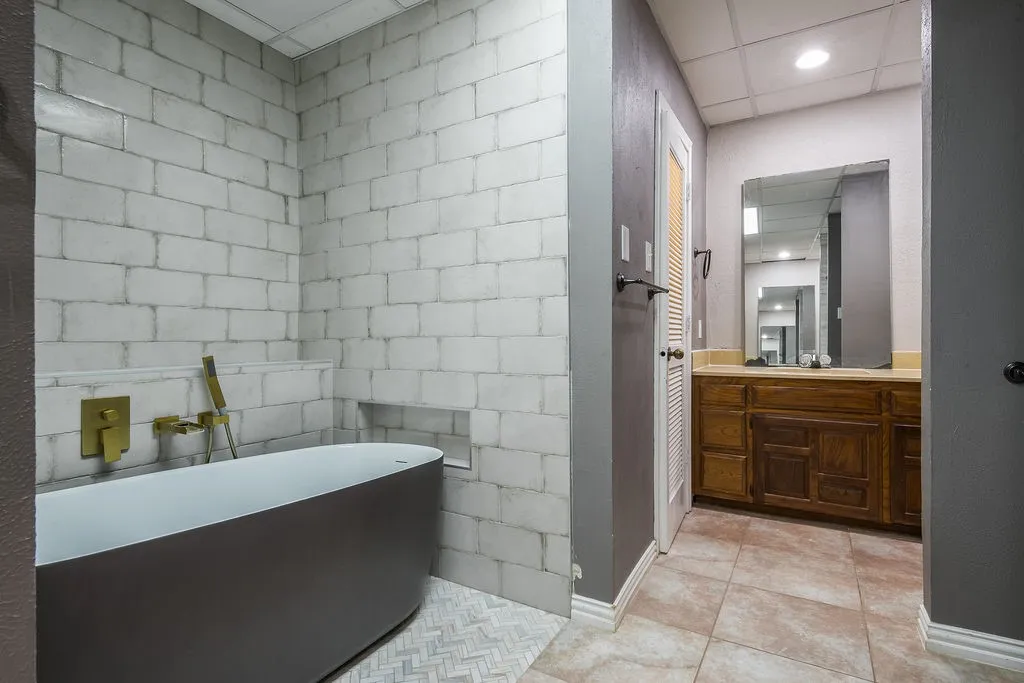 Freestanding soaking tub with matte black finish, gold-tone fixtures, and white subway tile surround